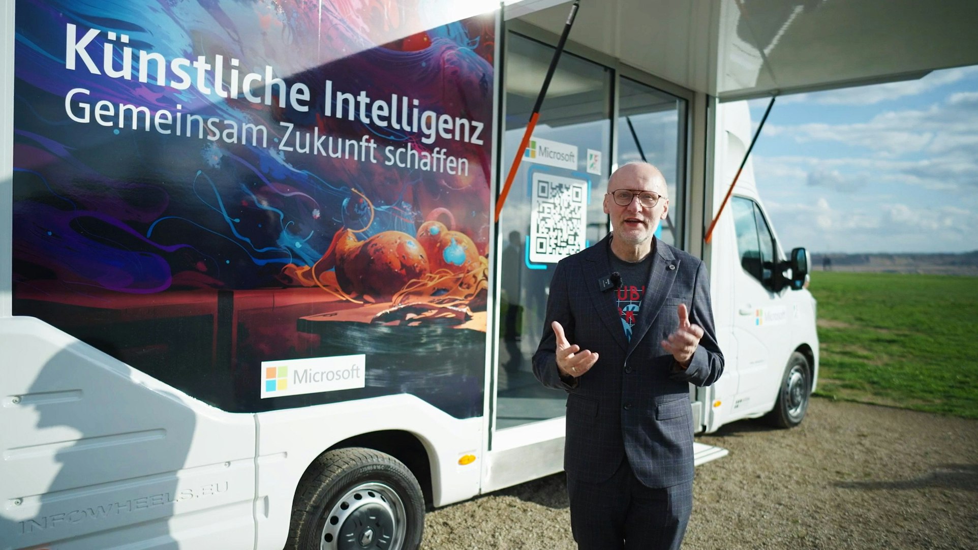 Ein Mann steht vor einem Fahrzeug, darauf ist der Hinweis „Künstliche Intelligenz - Gemeinsam Zukunft schaffen“ zu lesen.