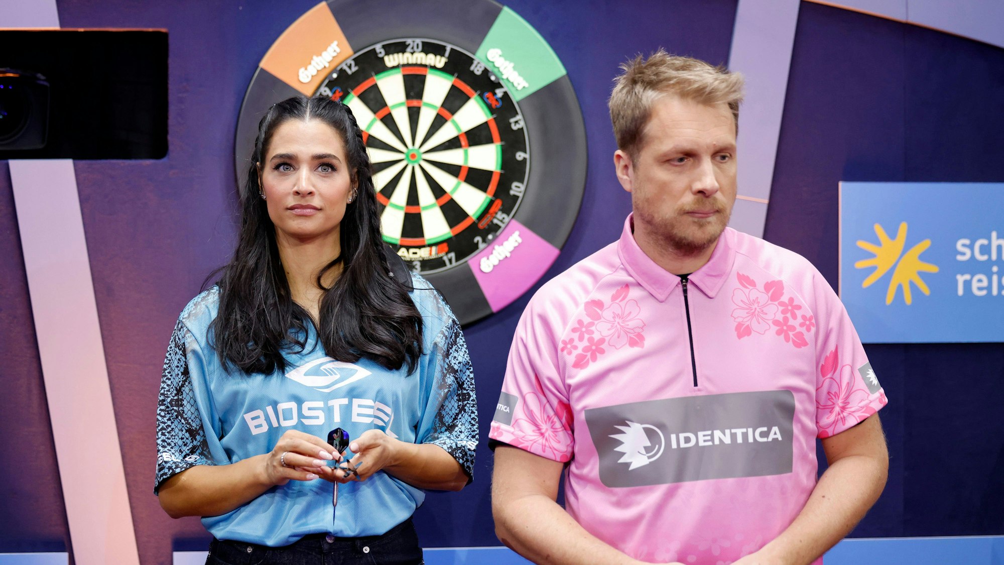 Amira Aly und Oliver Pocher stehen vor Dartscheiben.