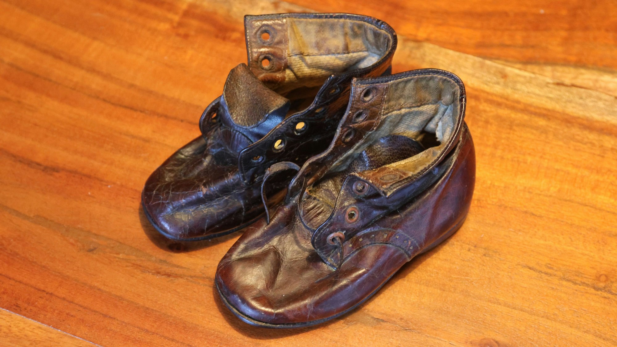 Alte Kinderschuhe aus Leder stehen auf einem Tisch.