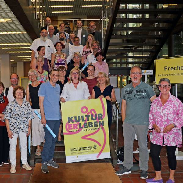 Viele Männer und Frauen lächeln in die Kamera. Zwei Frauen halten ein Schild mit der Aufschrift „KULTURERLEBEN “in ihren Händen.