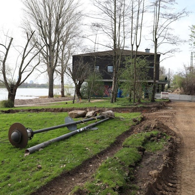 Auf einer Wiese lagern Straßenlaternen, die Bauarbeiten am Rheinradweg ruhen.
