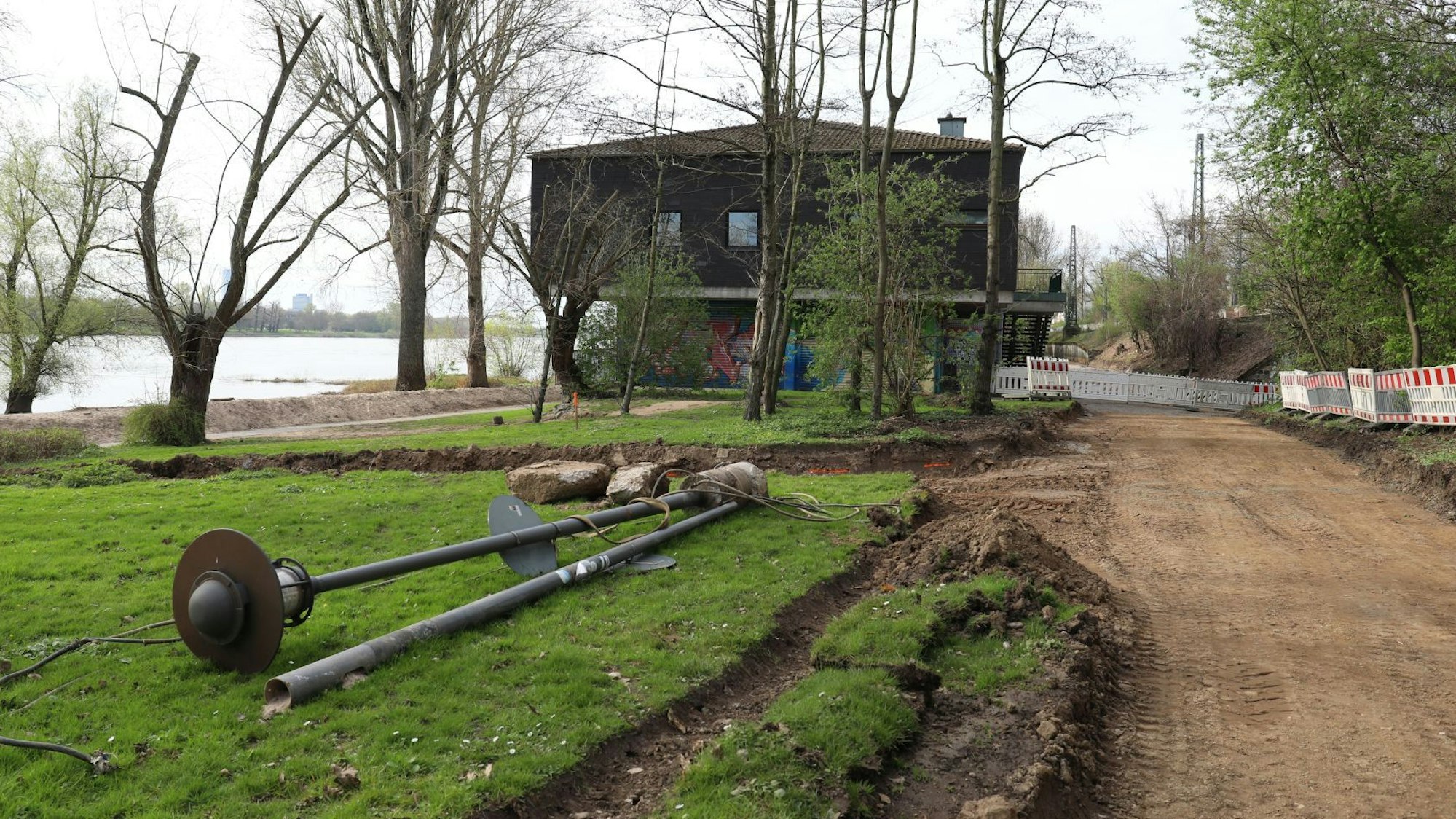 Auf einer Wiese lagern Straßenlaternen, die Bauarbeiten am Rheinradweg ruhen.
