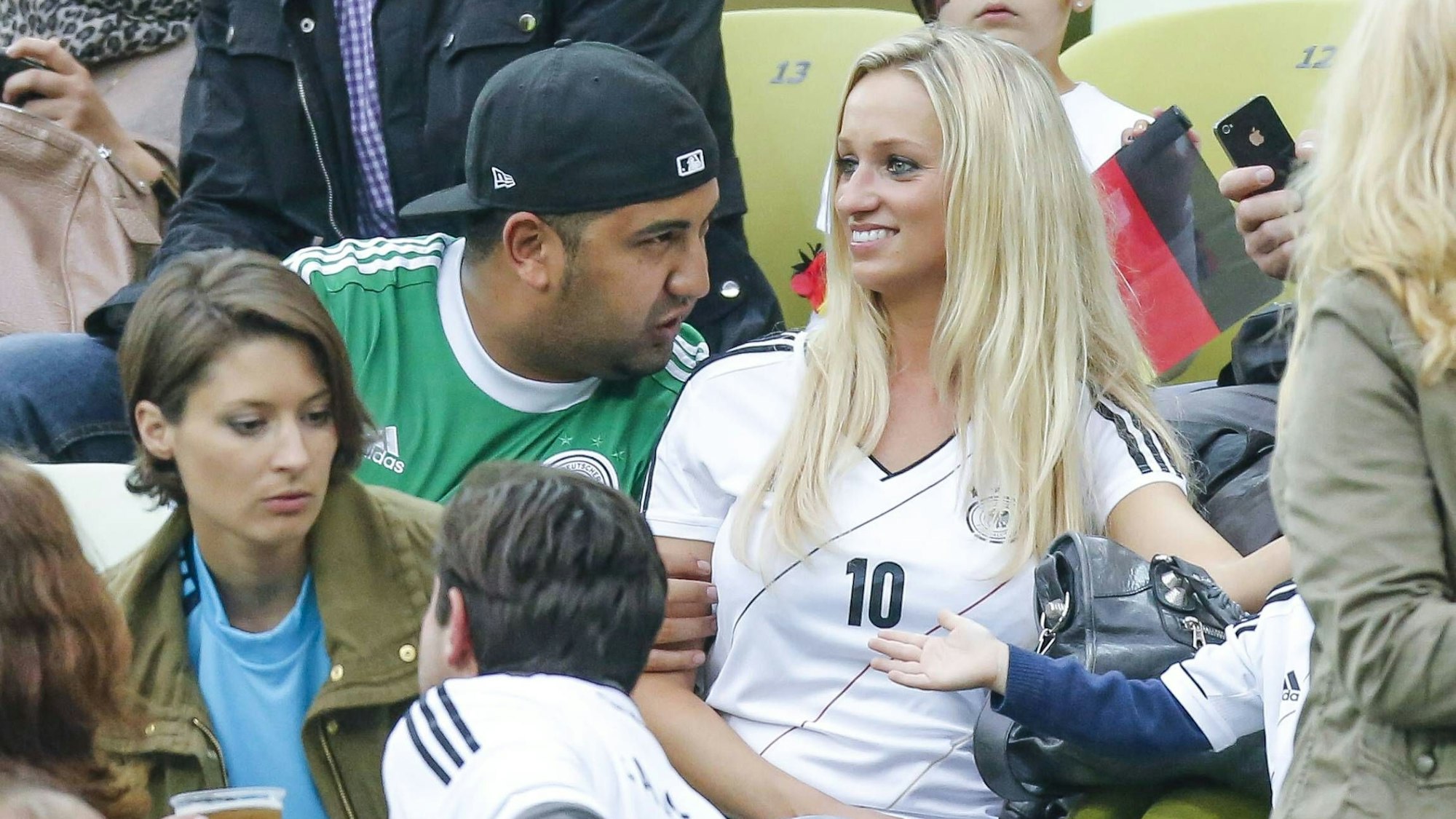 Monika Puchalski, Ehefrau von Lukas Podolski, lacht mit Trikot und Sohn Louis, auf der Ehrentribüne.