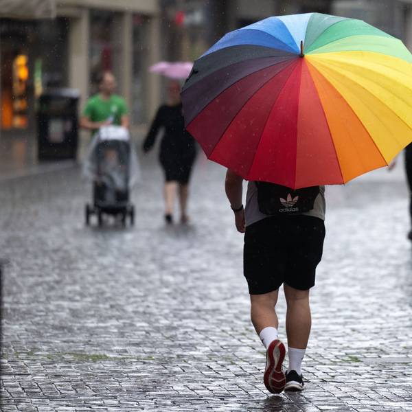 Ein Mann mit buntem Regenschirm geht durch eine Fußgängerzone.