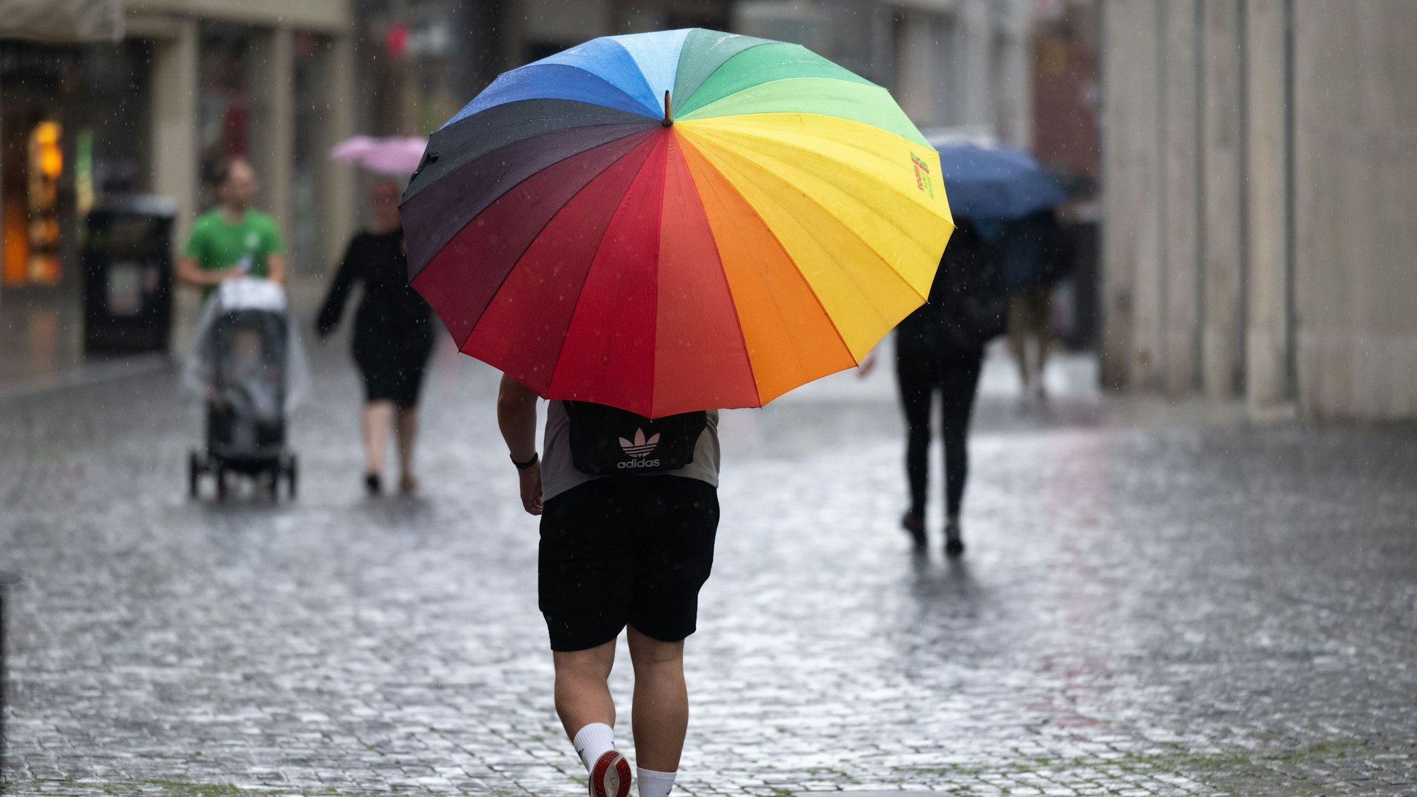 Ein Mann mit buntem Regenschirm geht durch eine Fußgängerzone.