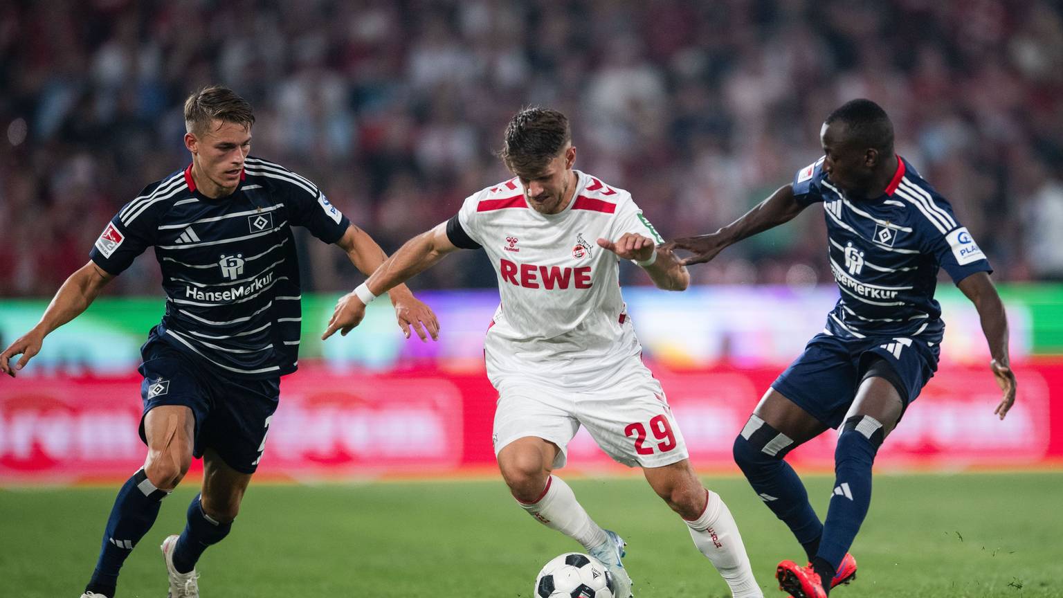 Hamburgs Miro Muheim (l) und Jean-Luc Dompe (r) kämpfen mit Kölns Jan Thielmann um den Ball.