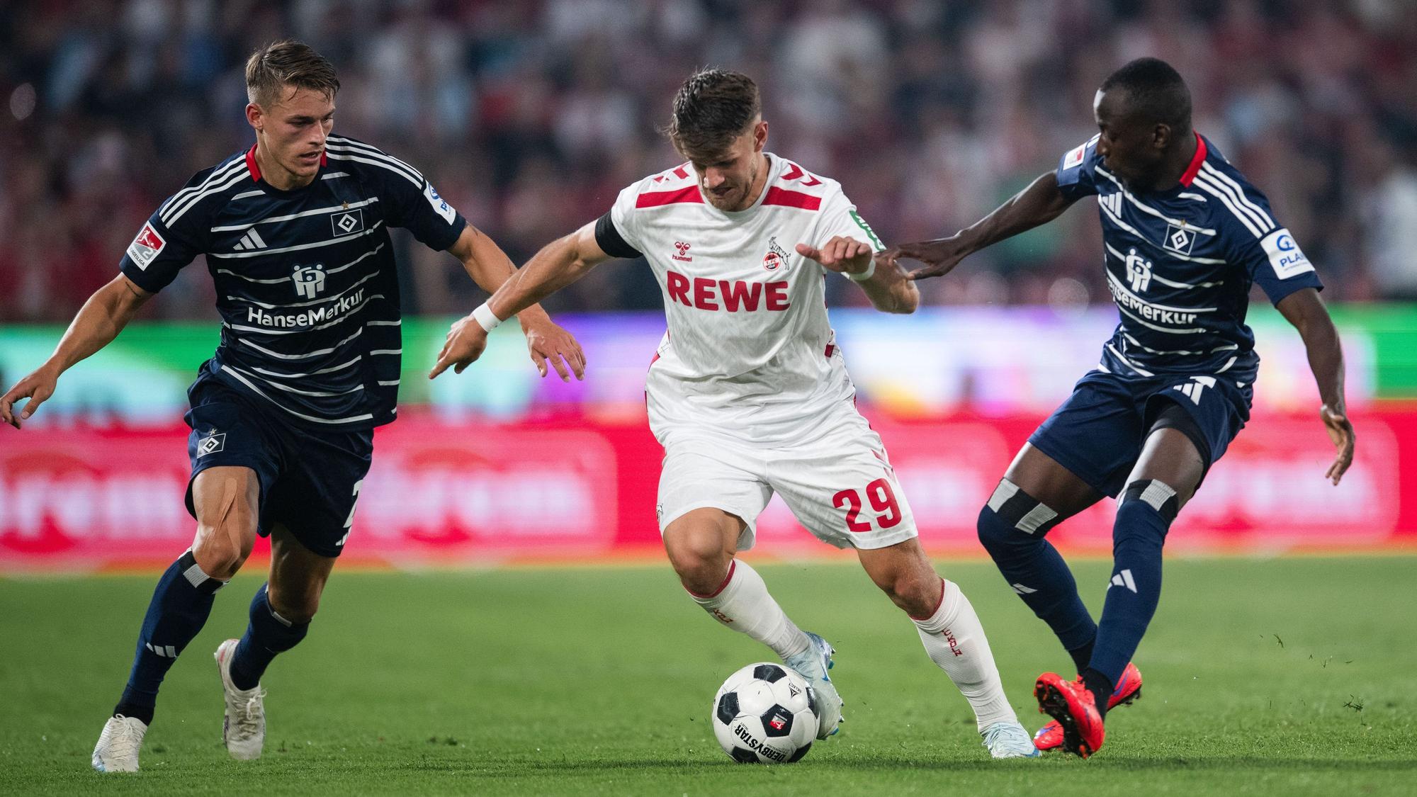Hamburgs Miro Muheim (l) und Jean-Luc Dompe (r) kämpfen mit Kölns Jan Thielmann um den Ball.