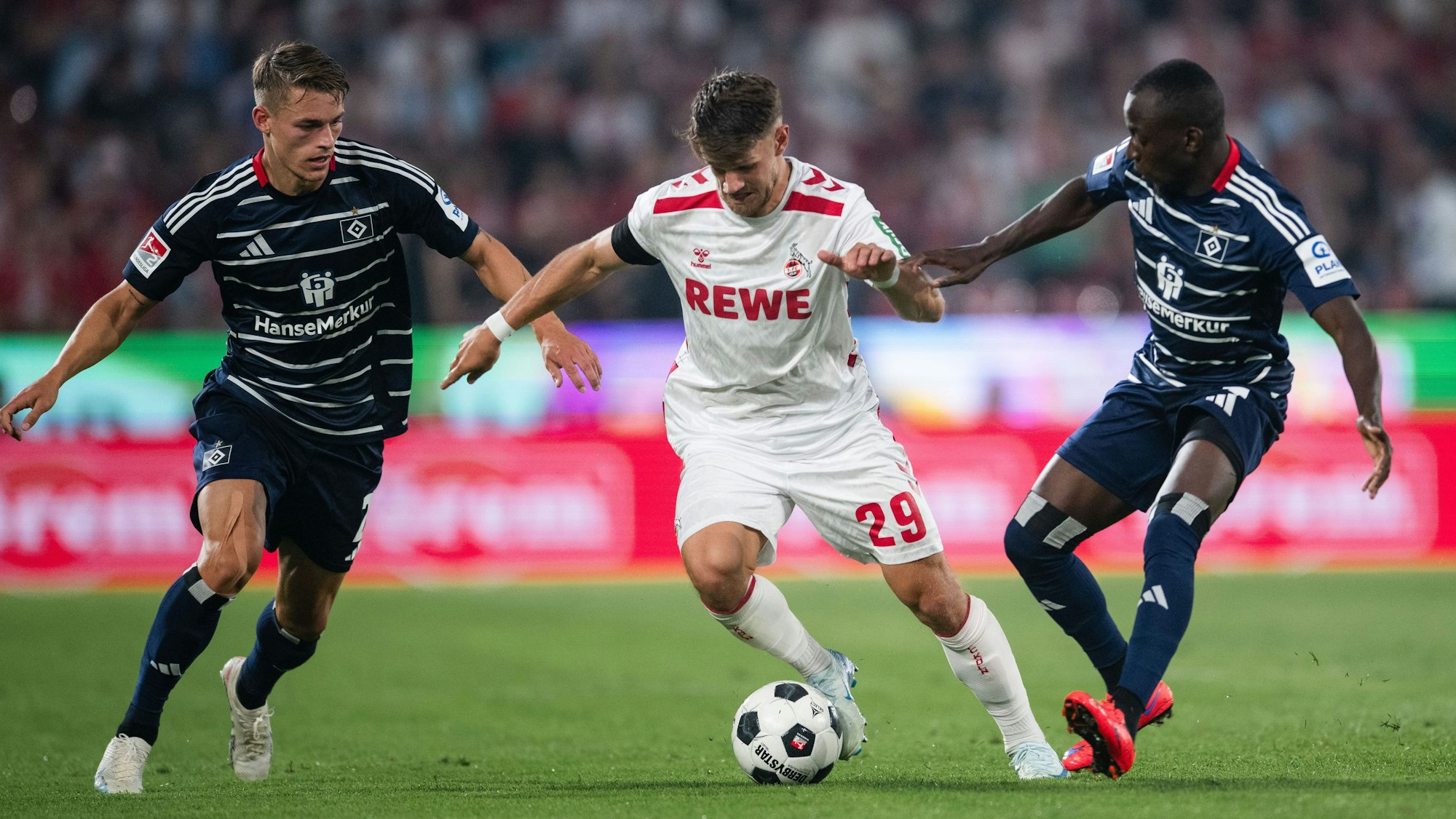 Hamburgs Miro Muheim (l) und Jean-Luc Dompe (r) kämpfen mit Kölns Jan Thielmann um den Ball.