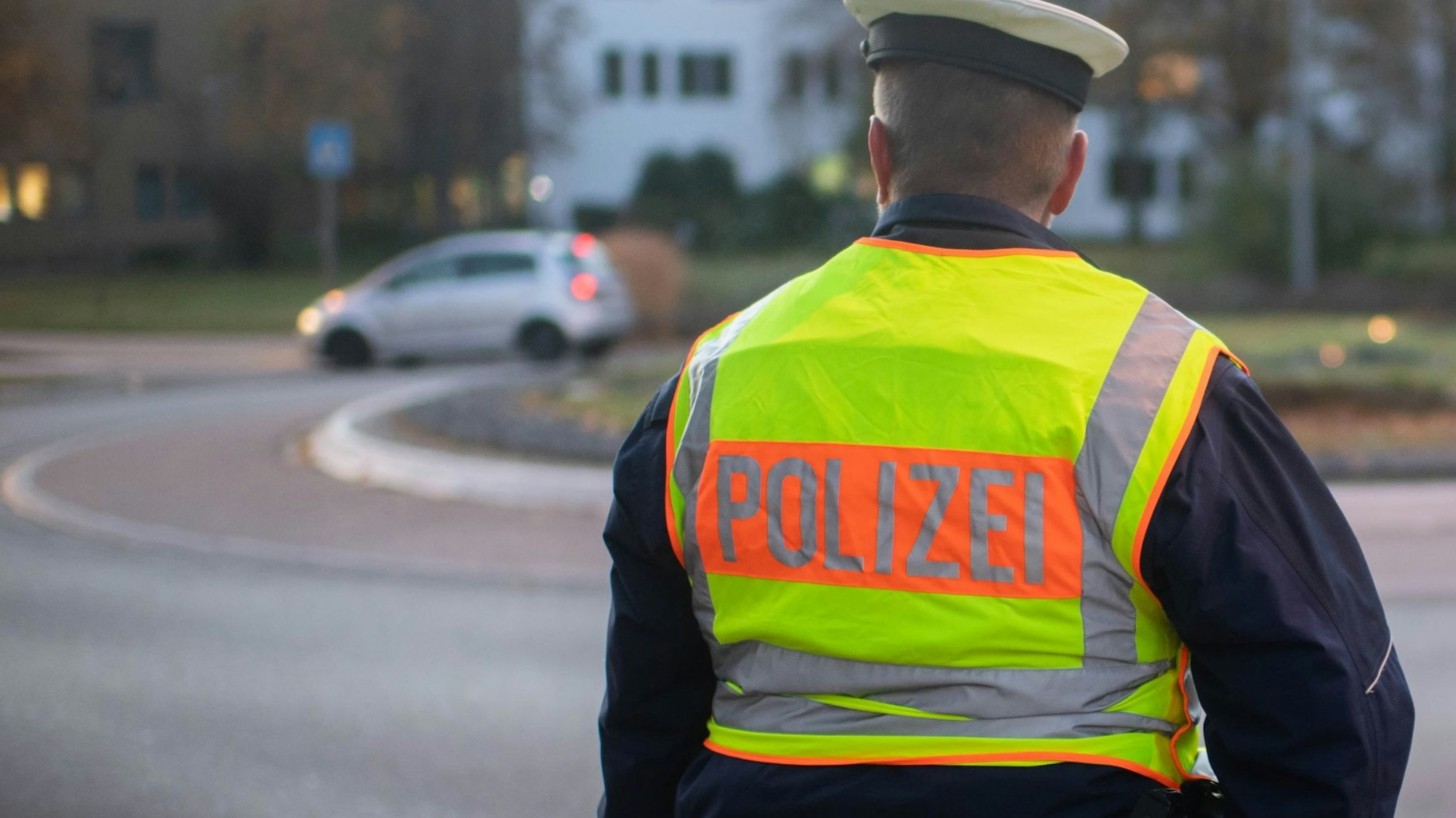 Das Symbolbild zeigt einen Polizisten, der an einem Kreisverkehr steht und einem vorbeifahrenden Auto hinterherschaut.