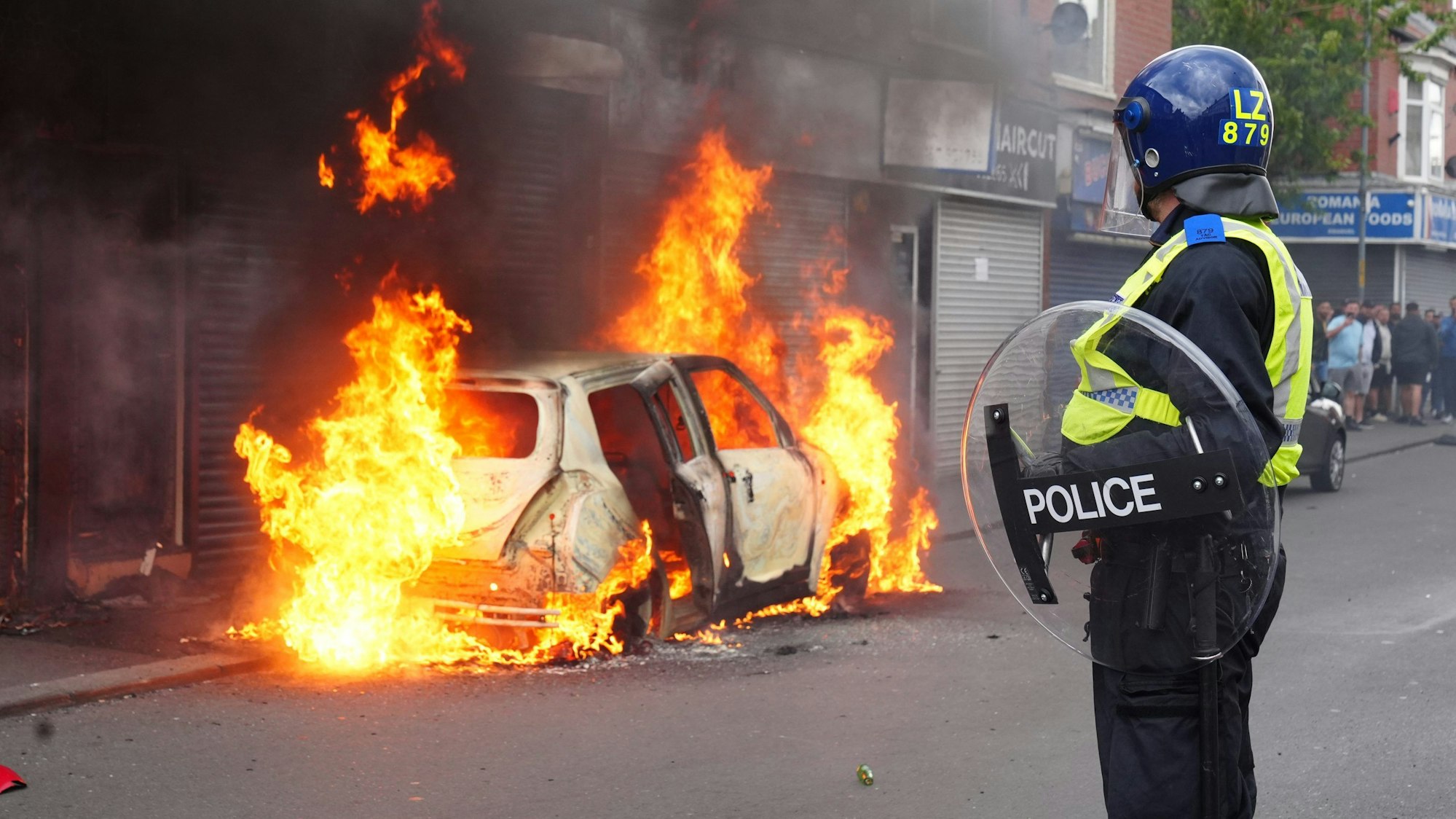 Ein Polizist blickt auf ein brennendes Auto auf der Parliament Road während einer Anti-Einwanderungsdemonstration.