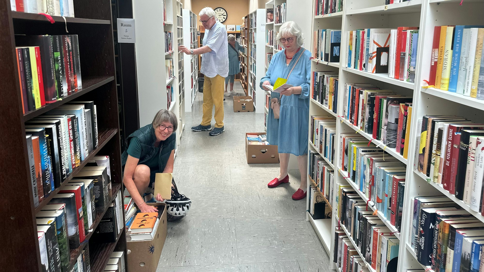 Frauen und Männer suchen in Regalen nach Büchern.