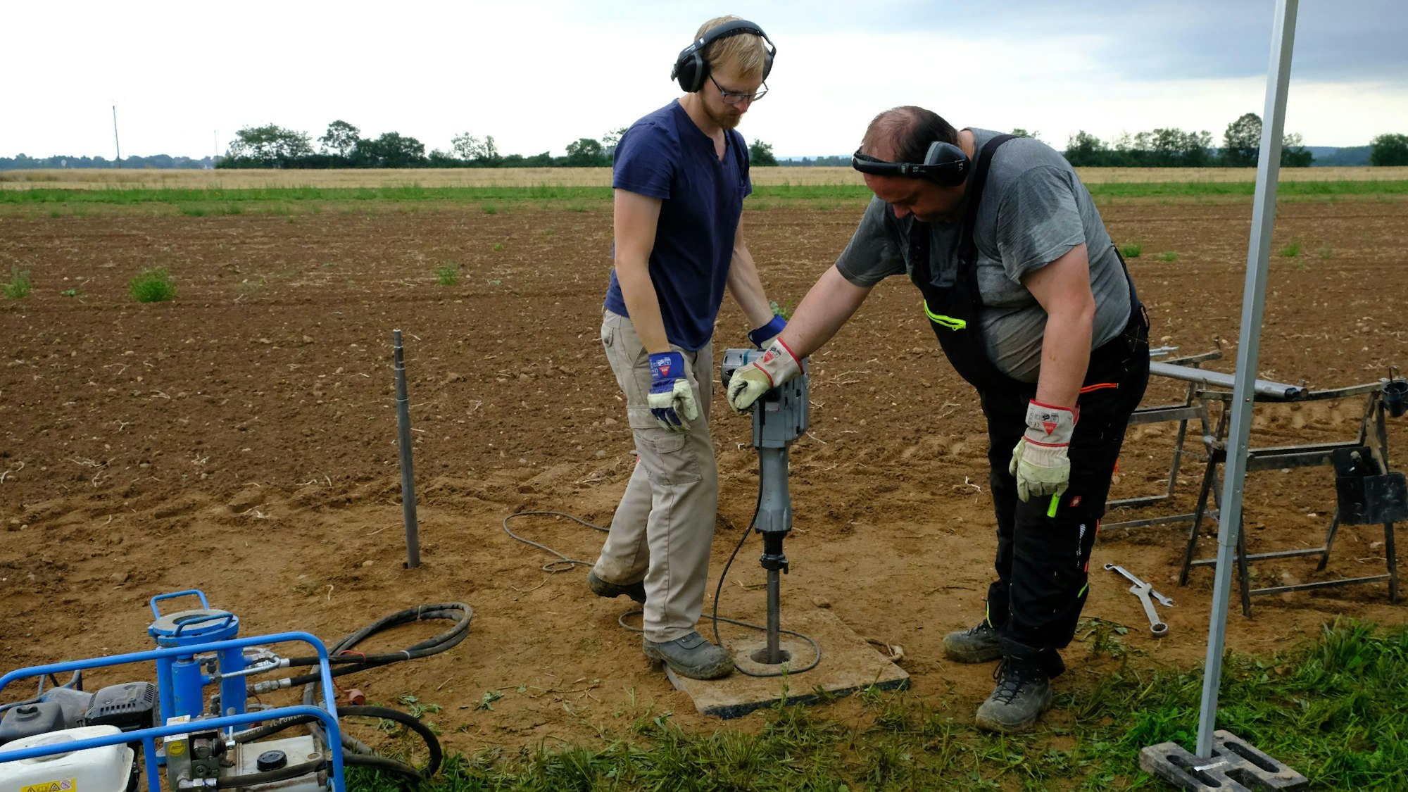 Zwei Mitarbeiter des Geologischen Dienstes führen eine Erdbohrung auf einem Acker durch.