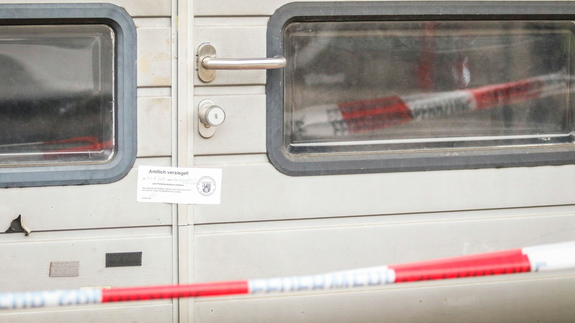 Vor einer silbernen Tür ist ein rot-weißes Flatterband angebracht. An der Tür ist ein Siegel der Polizei angebracht.
