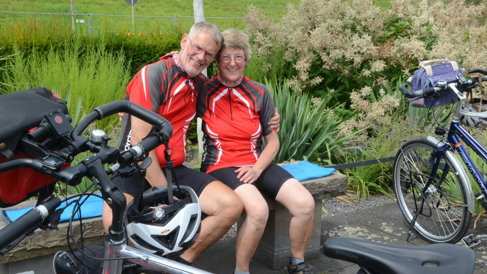 Ein Mann und eine Frau in Fahrradkleidung sitzen auf einer Bank.