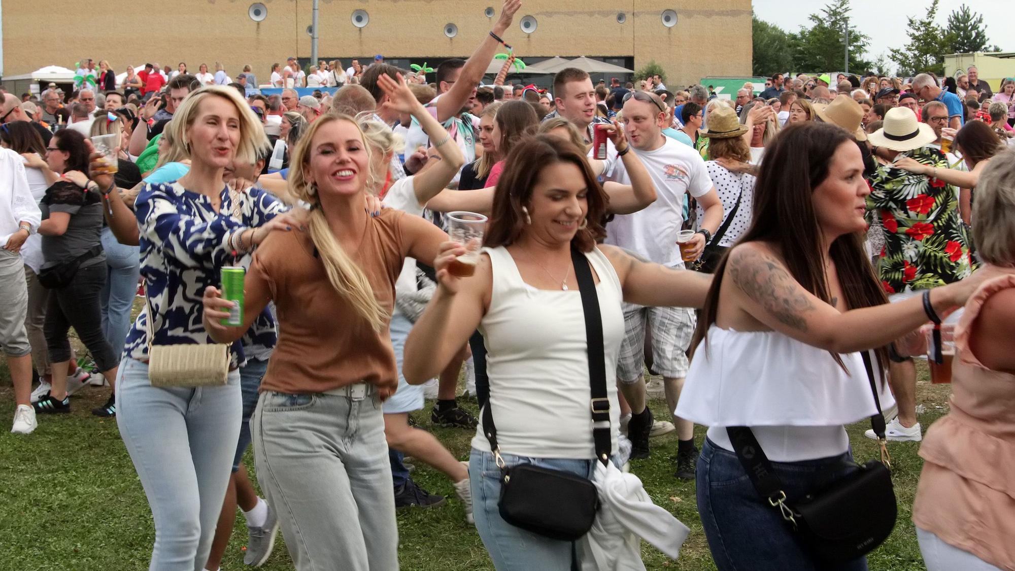 Frauen und Männer tanzen auf einer Wiese ausgelassen.
