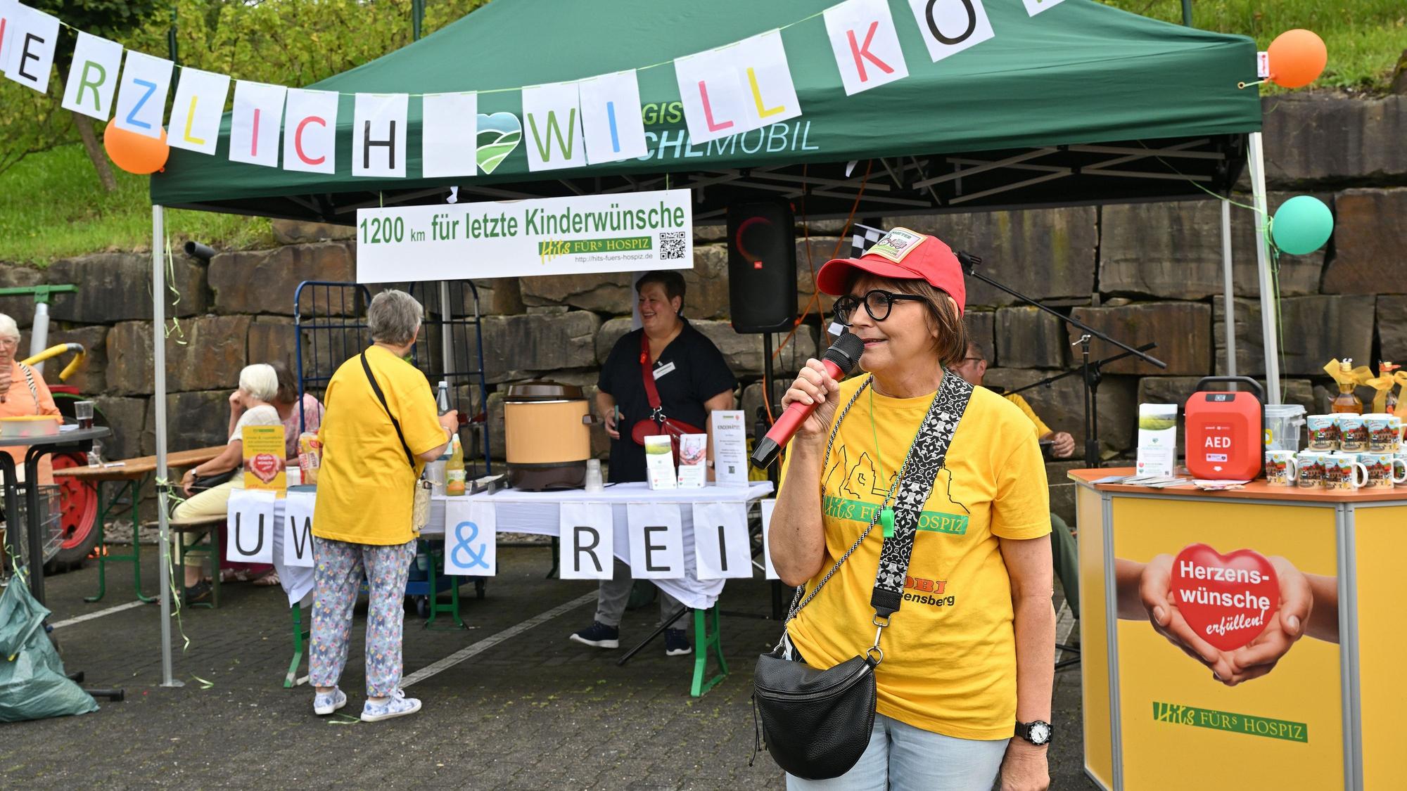 Eine Frau spricht in ein Mikro, im Hintergrund ist ein Banner mit der Aufschrift „Herzlich Willkommen“ zu sehen.