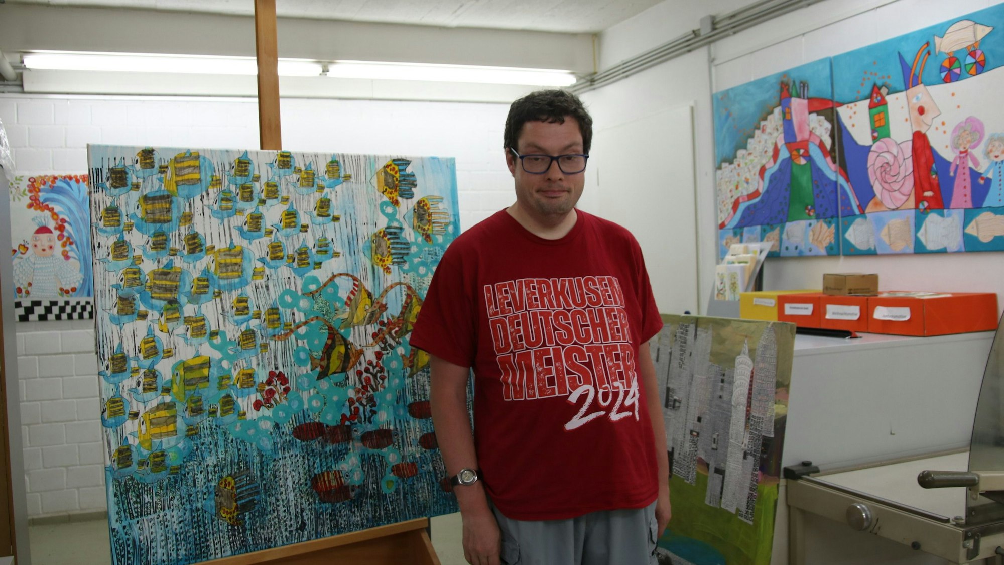 Ein Mann in rotem T-Shirt vor einem Bild, das viele Fische zeigt.