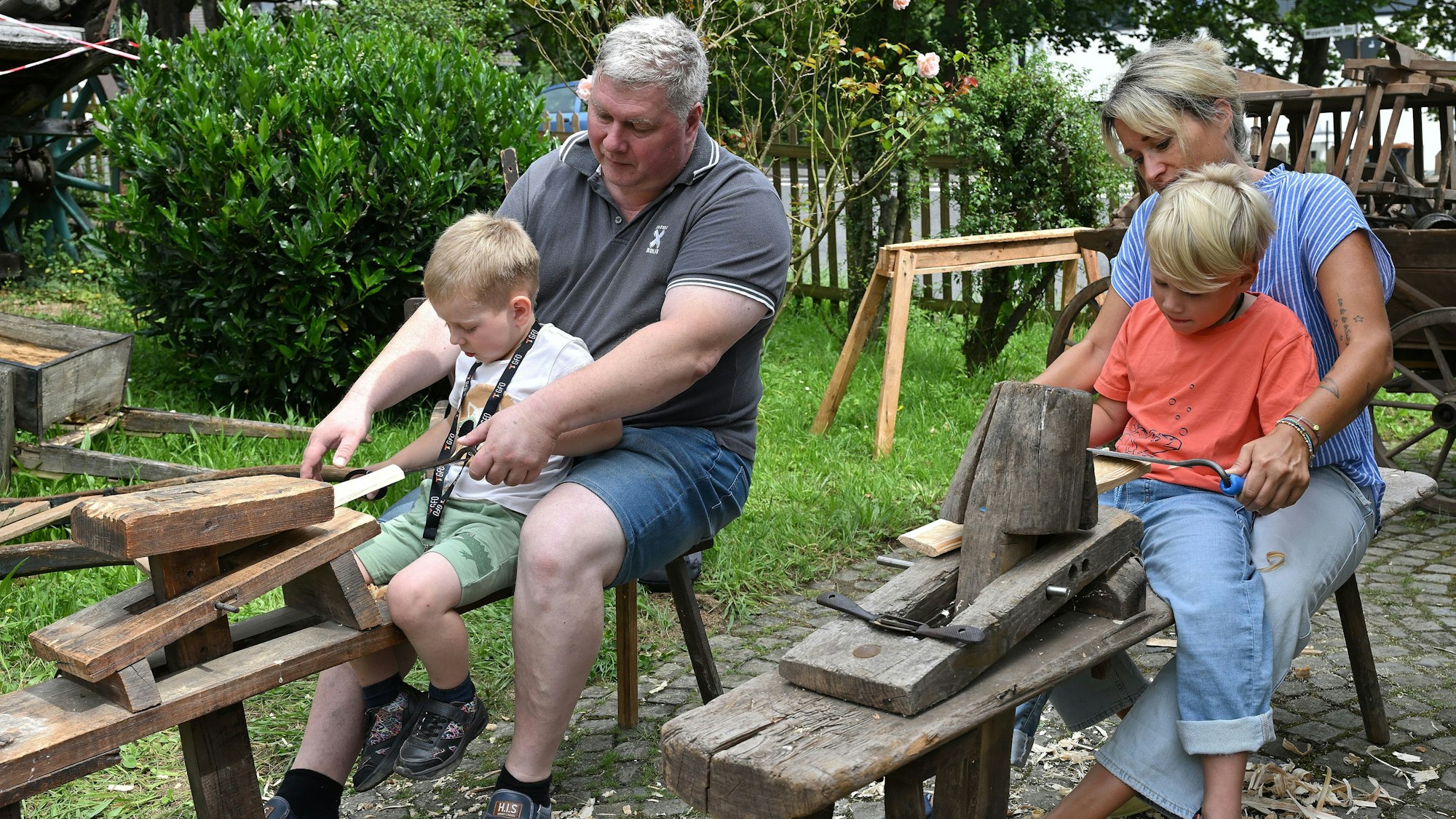 Erwachsene stellen mit Kindern Holzschindeln her.