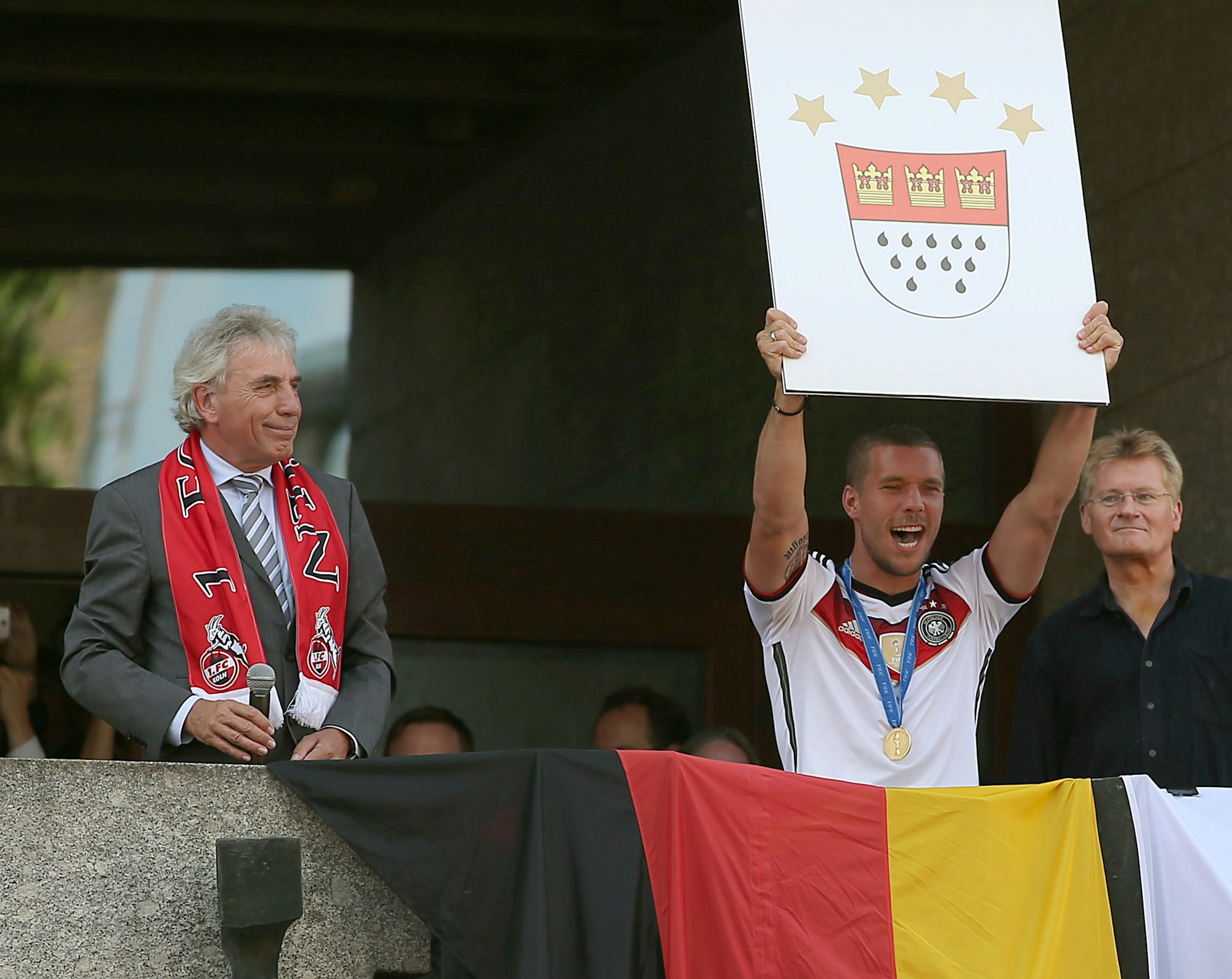 Fußball-Weltmeister Lukas Podolski (M) jubelt am 16.07.2014 in Köln (Nordrhein-Westfalen) auf dem Balkon des Rathauses neben Oberbürgermeister Jürgen Roters (l). Nach