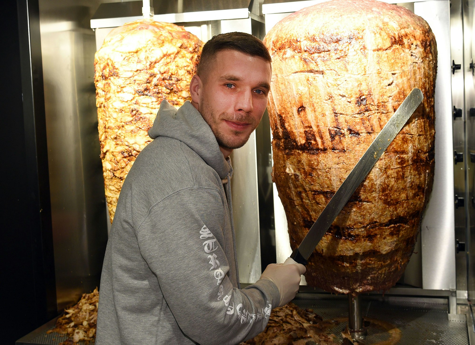 Lukas Podolski steht am 06.01.2018 in Köln  bei der Eröffnung eines Döner-Ladens an einem Dönerspieß.