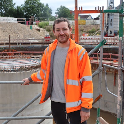 Ein Mann mit orangefarbener Warnjacke auf einer Baustelle.