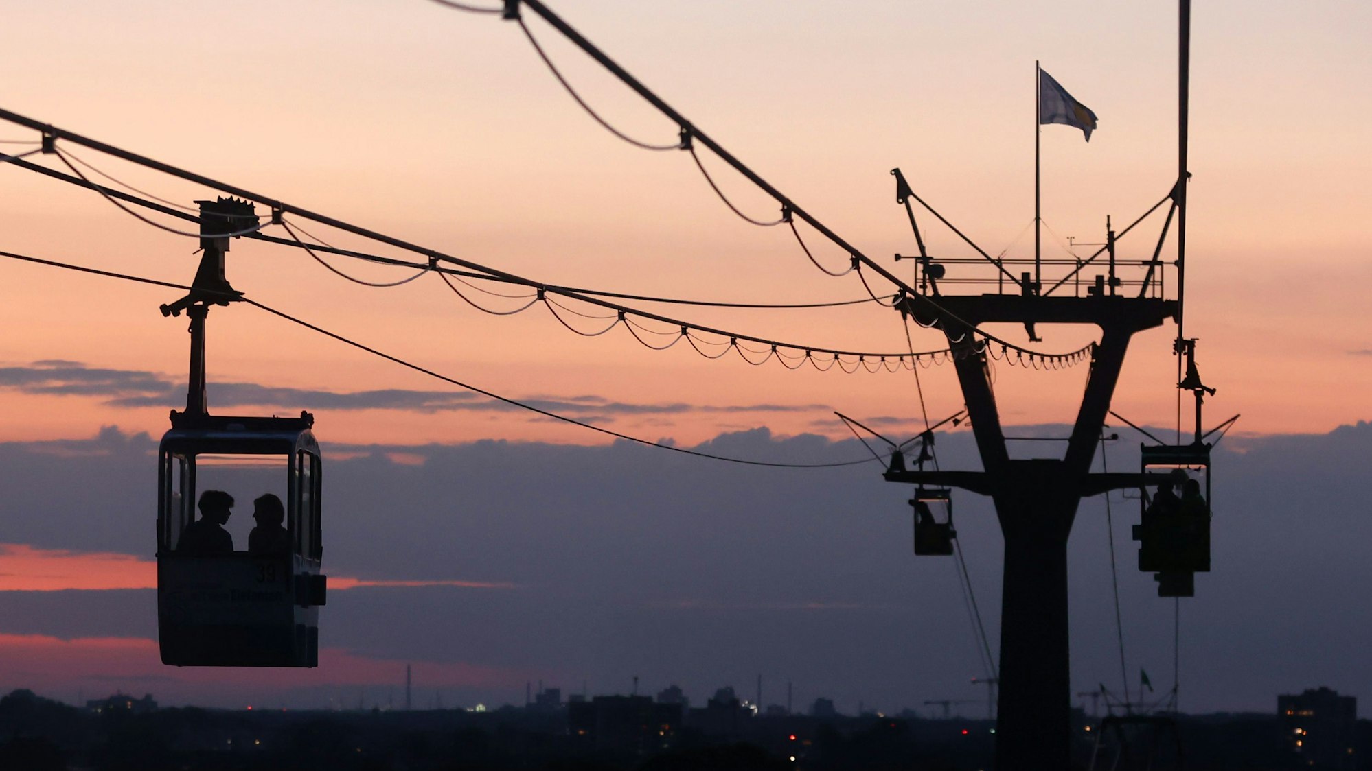 Bei einem orangeroten Himmel fährt die Kölner Seilbahn über den Rhein. In Köln könnten spätestens in der kommenden Woche nochmal mehr als 30 Grad erreicht werden. Erste Wettermodelle rechnen mit tropischen Temperaturen. (Symbolbild)