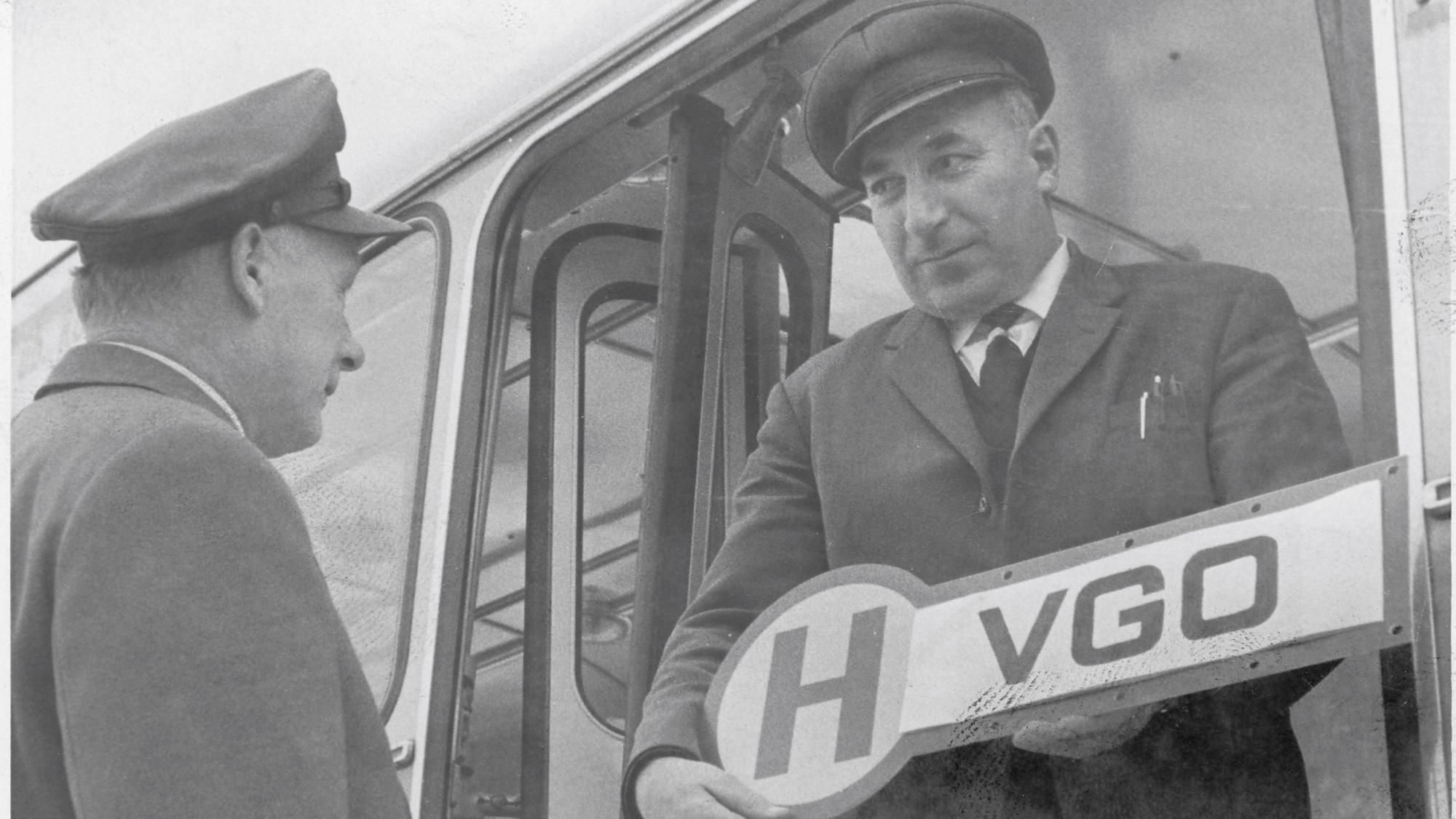 Historisches Foto von zwei Männern mit einem Bushaltestellenschild in den Händen.