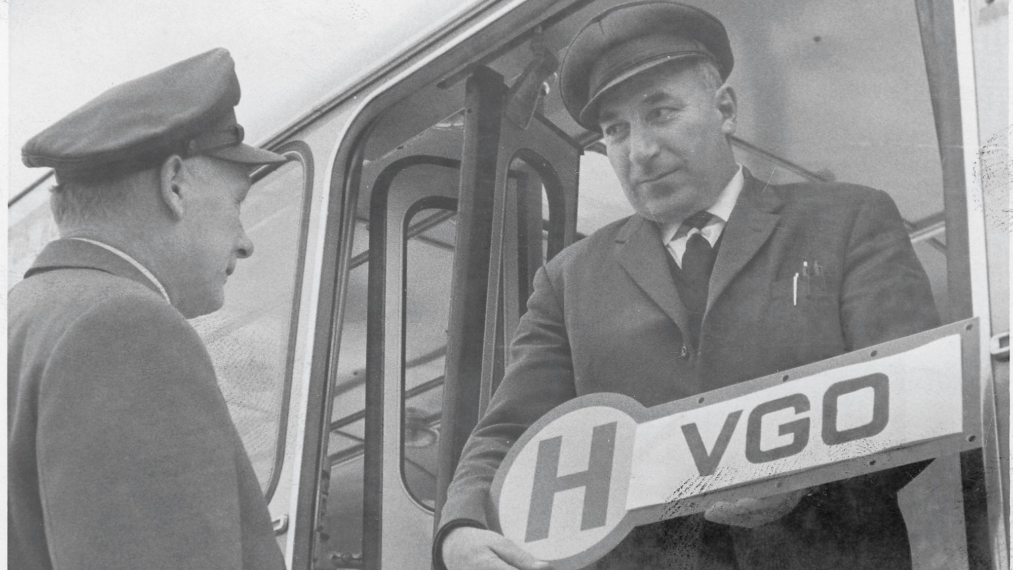 Historisches Foto von zwei Männern mit einem Bushaltestellenschild in den Händen.