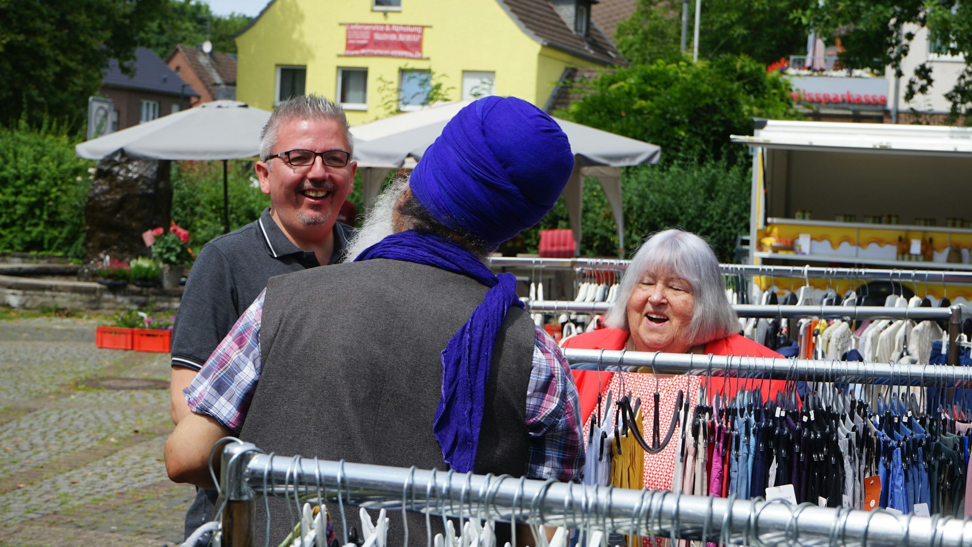 Auf dem Marktplatz in Türnich unterhält sich David Held (BBK) mit einem Verkäufer und Anwohnerin Sybille Fischer.