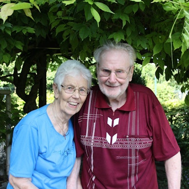 Das Pärchen lächelt in die Kamera. Fritz Jaeger trägt ein rotes Hemd mit weißen Mustern. Käthe Jaeger trägt eine hellblaue Bluse. Im Hintergrund einige Bäume.