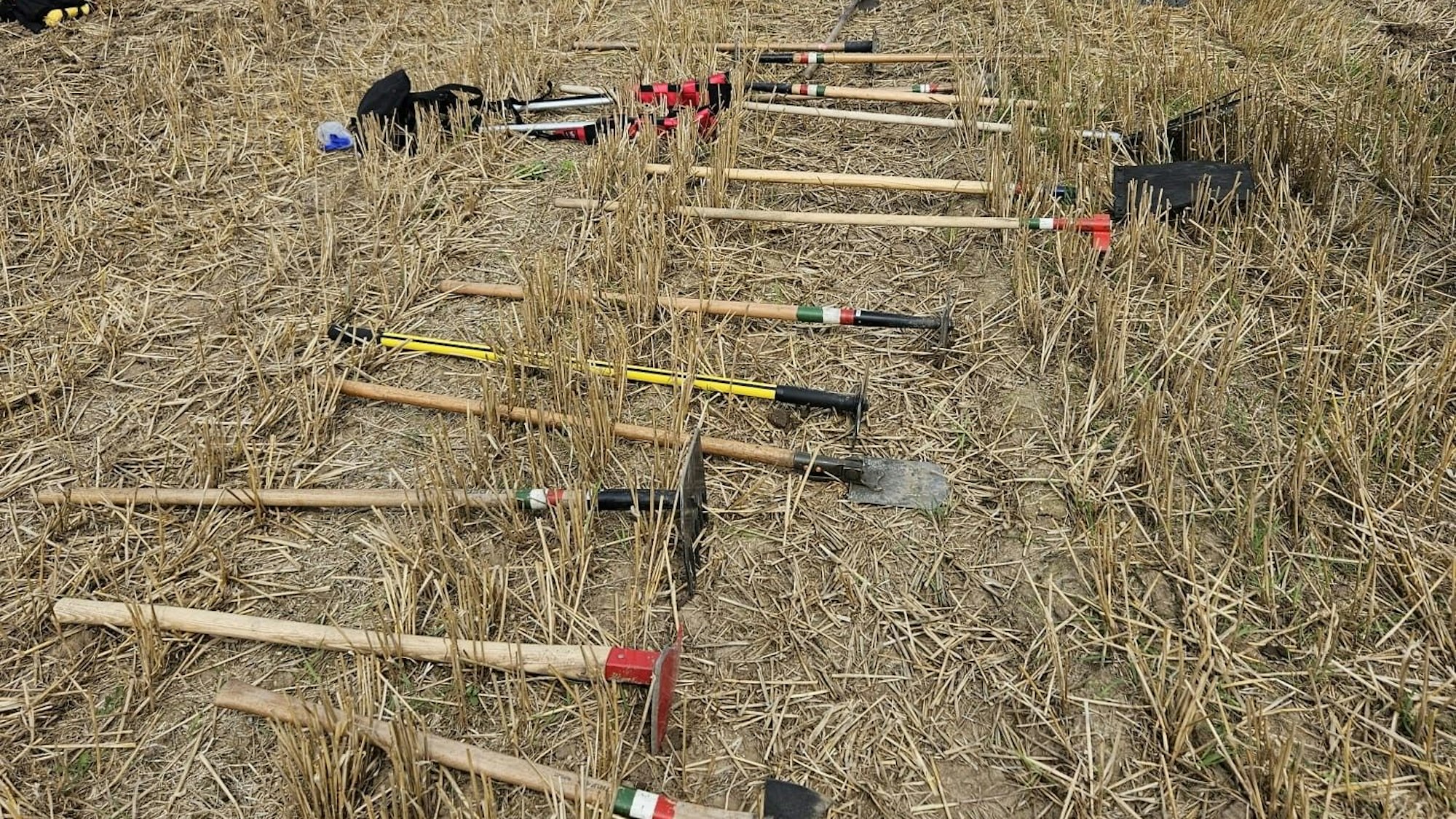 Feuerwehrwerkzeug liegt aufgereiht auf einem Stoppelfeld.