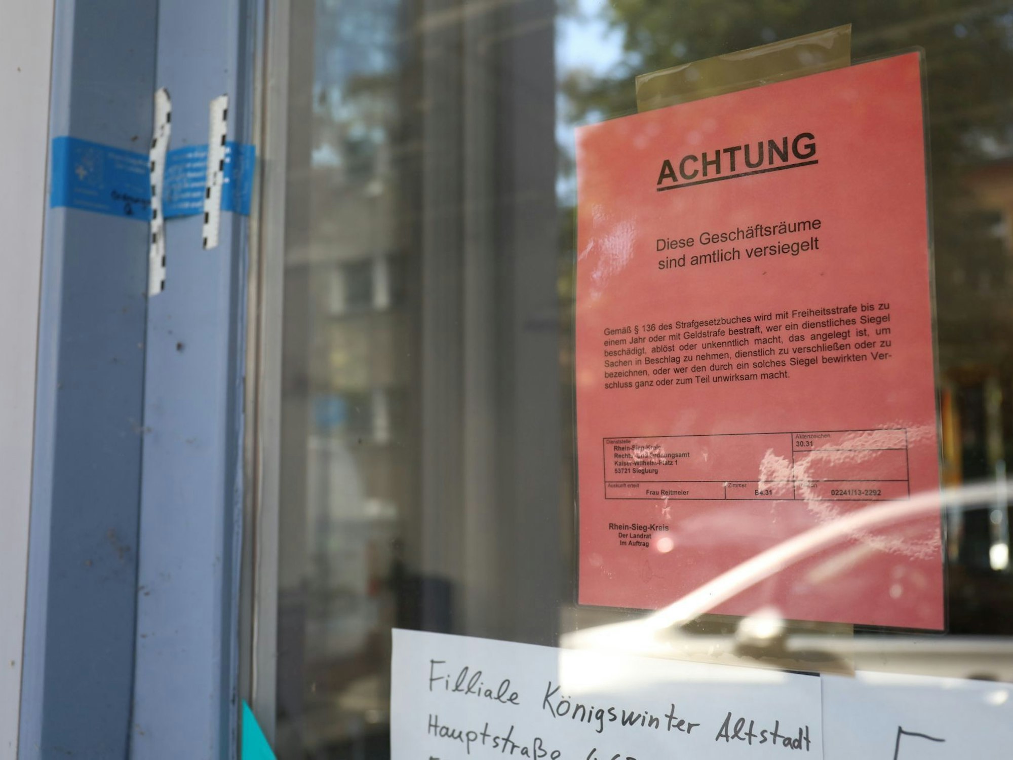 Ein Schaufenster mit einem roten Hinweiszettel und eine versiegelte Tür