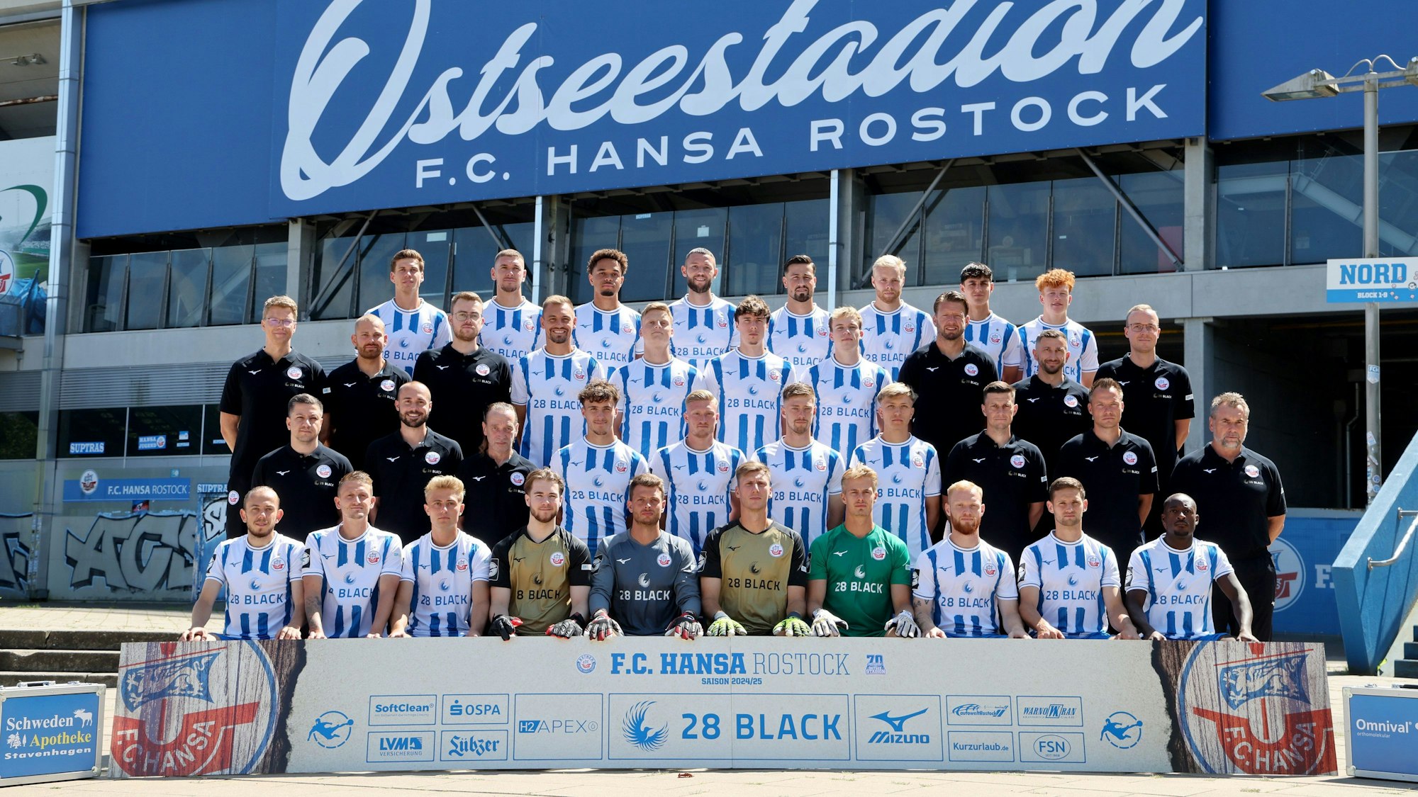 Die Mannschaftsmitglieder des Fußball-Drittligisten FC Hansa Rostock stehen bei einem Fototermin für ein Gruppenfoto nebeneinander vor dem Ostseestadion. Hauptsponsor „28 Black“ wirbt zwar weiter auf den Trikots, will die Partnerschaft mit dem Club aber vorzeitig beenden.