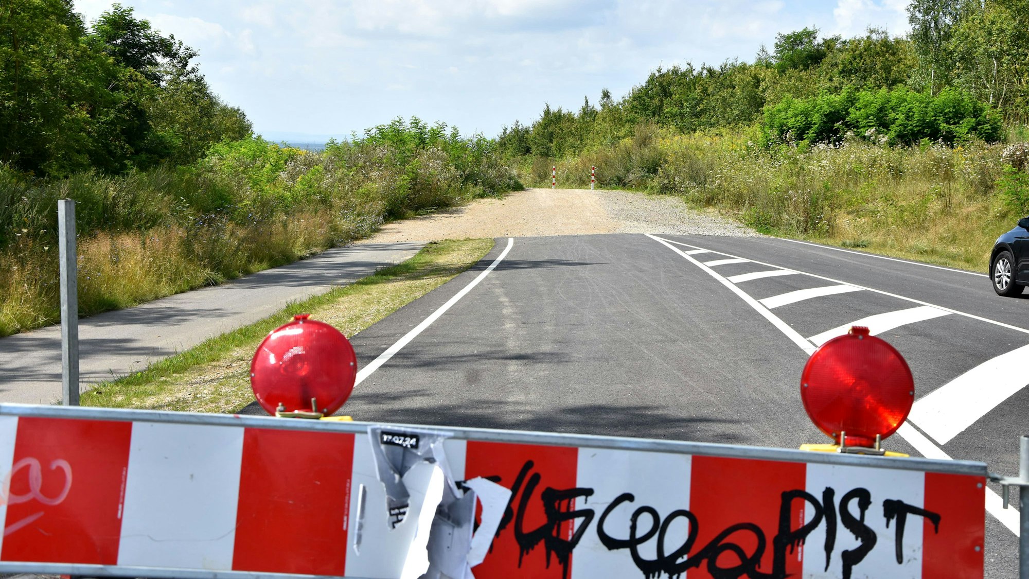 Eine rot-weiße Absperrbake, im Hintergrund ein Stück Straße, das an einem Weg endet.