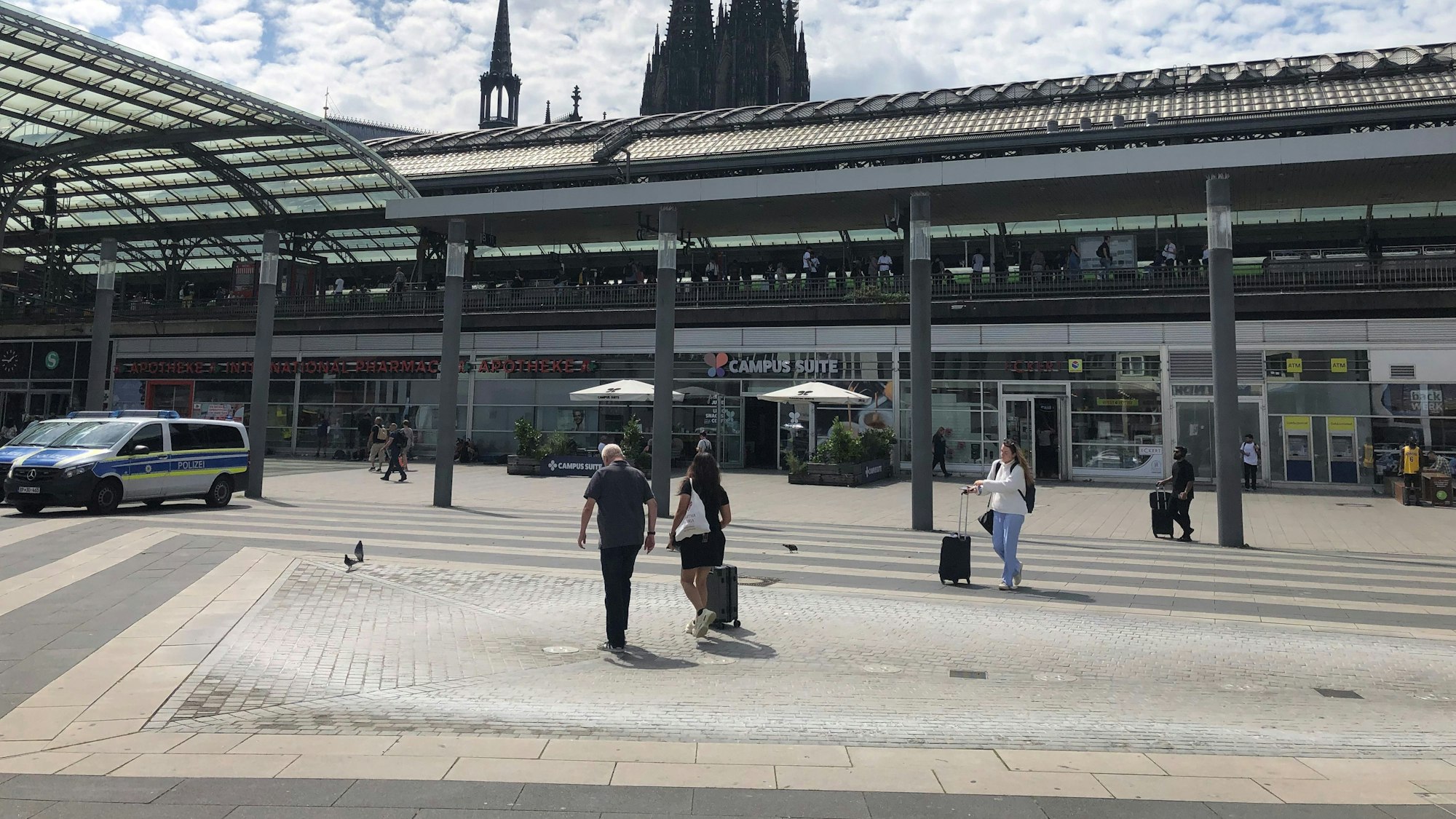 Passanten gehen durch den ausgetrockneten Springbrunnen auf dem Breslauer Platz in Köln.