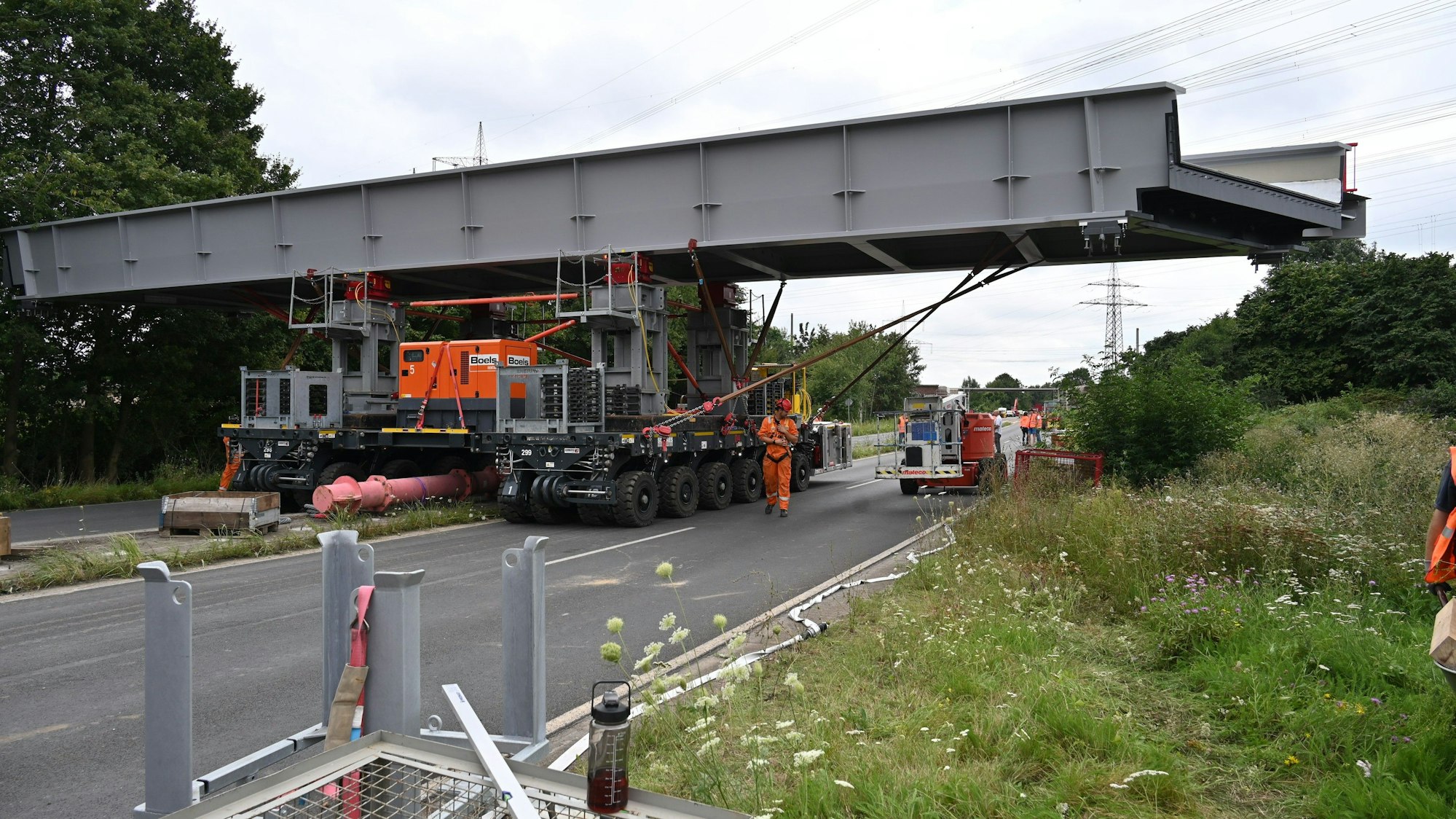 Zwei Transportfahrzeuge schieben das Stahlbrückenteil quer über die Fahrbahn.