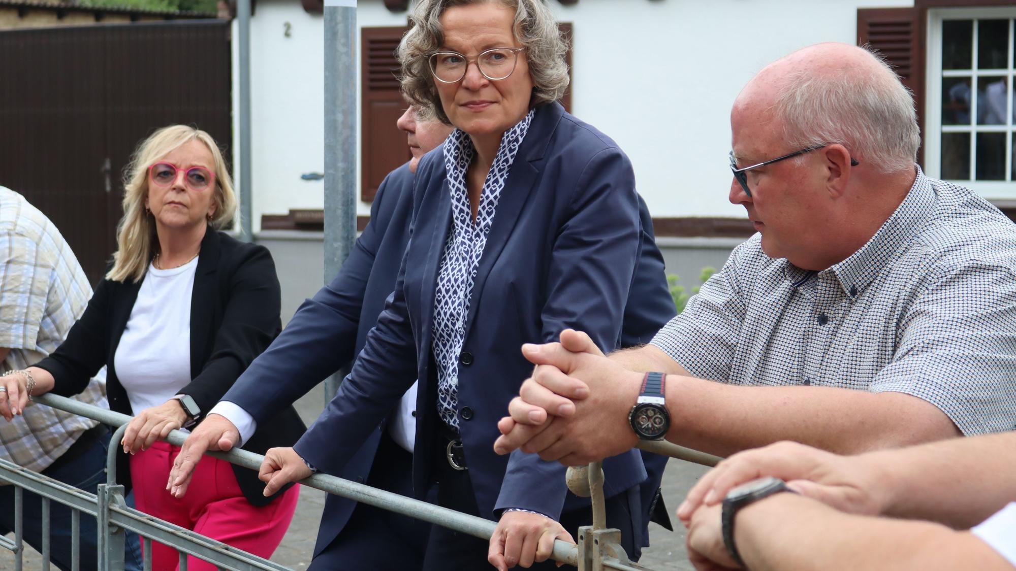 Ministerin Ina Scharrenbach lehnt sich an ein Geländer und schaut sich den Durchlass des Dreisbaches an.