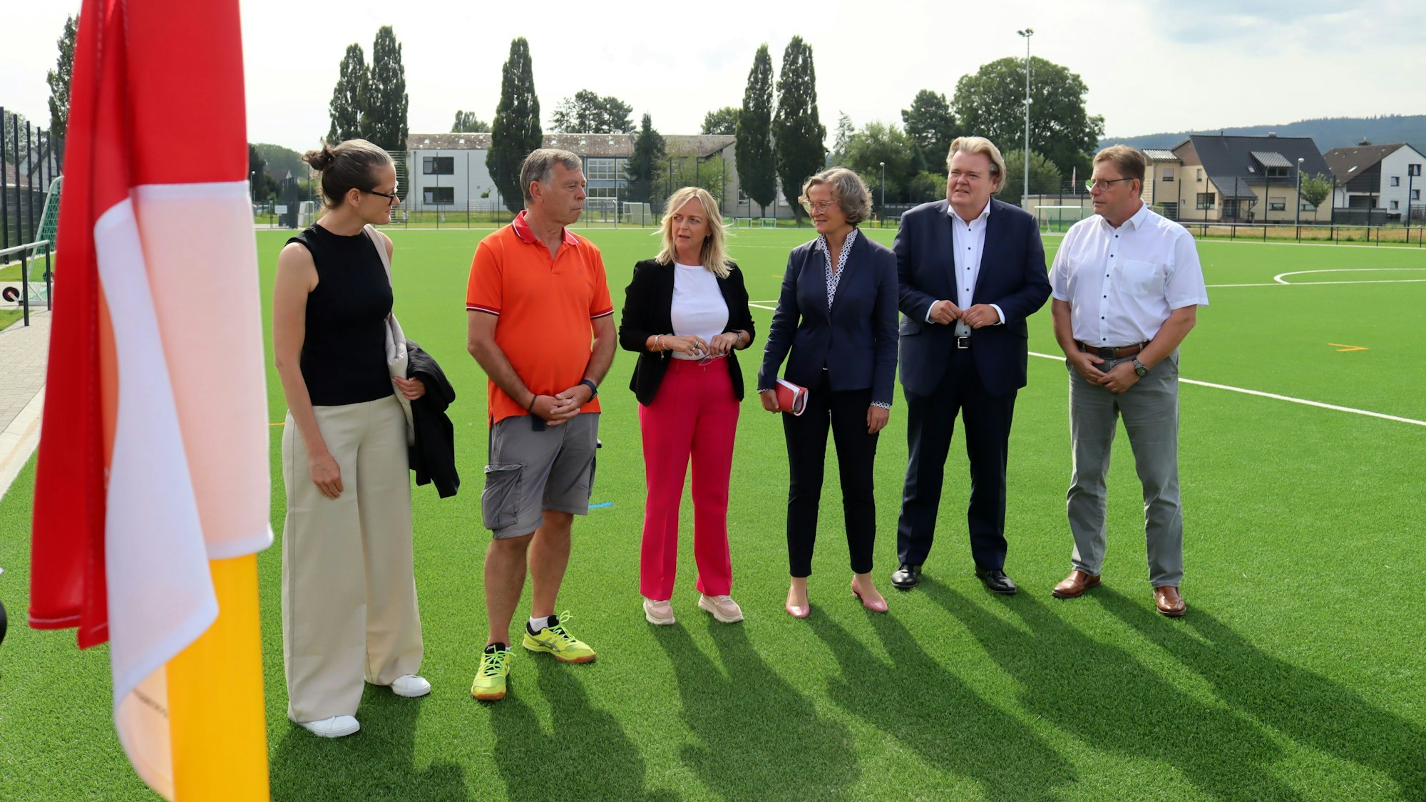 Sechs Menschen stehen auf dem neuen Kunstrasenplatz in Arloff. Im Vordergrund ist eine Eckfahne zu sehen.