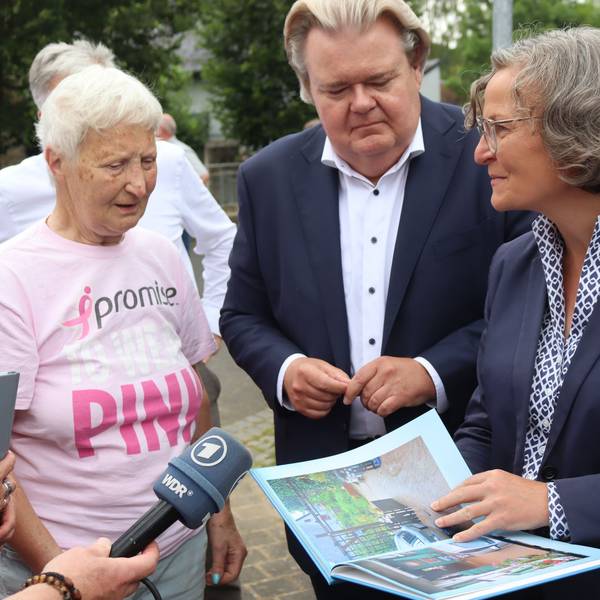 Ministerin Ina Scharrenbach hält ein Fotobuch in der Hand und redet mit Monika von der Osten aus Schönau.
