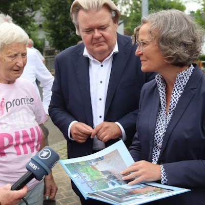 Ministerin Ina Scharrenbach hält ein Fotobuch in der Hand und redet mit Monika von der Osten aus Schönau.