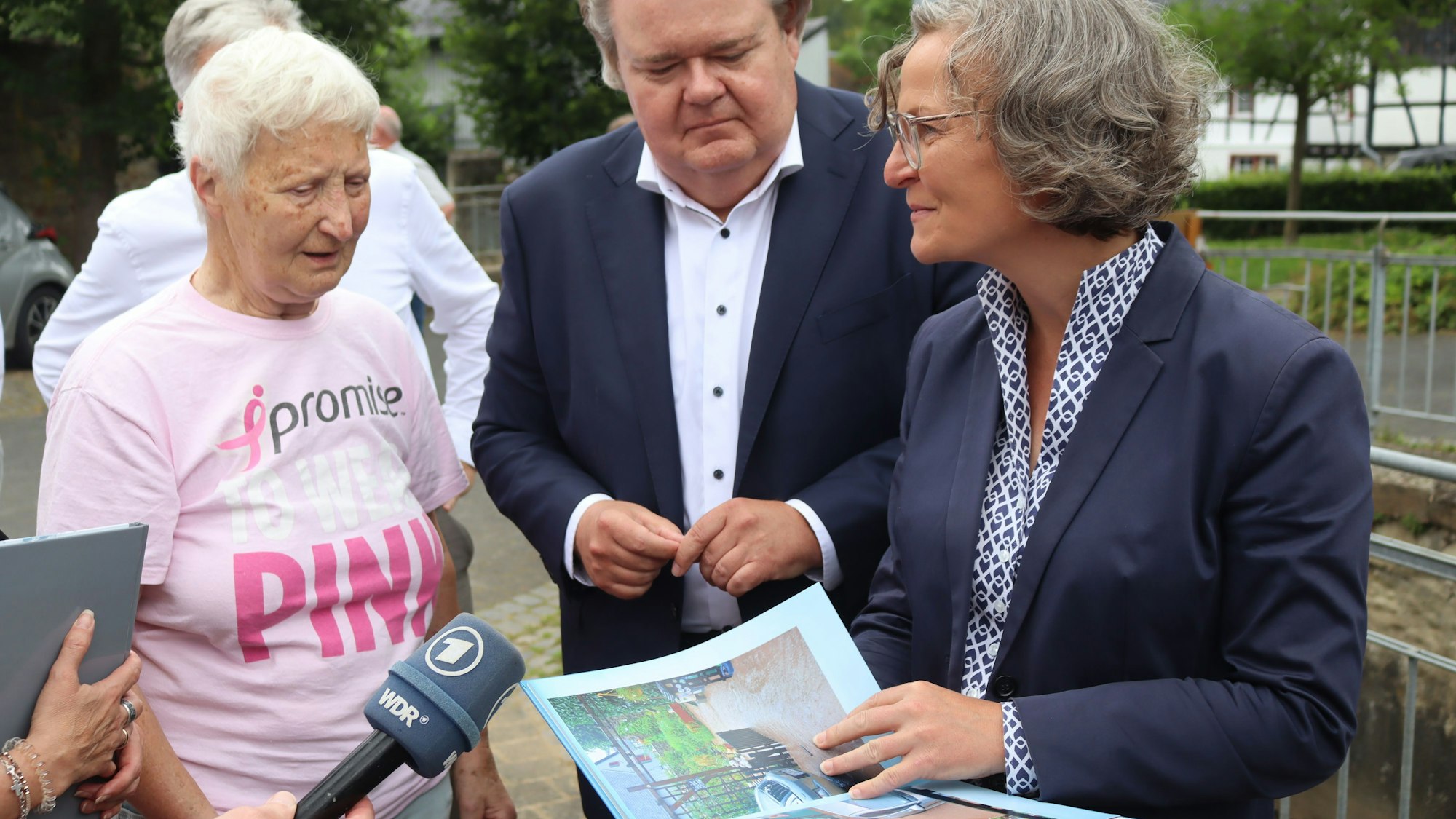 Ministerin Ina Scharrenbach hält ein Fotobuch in der Hand und redet mit Monika von der Osten aus Schönau.