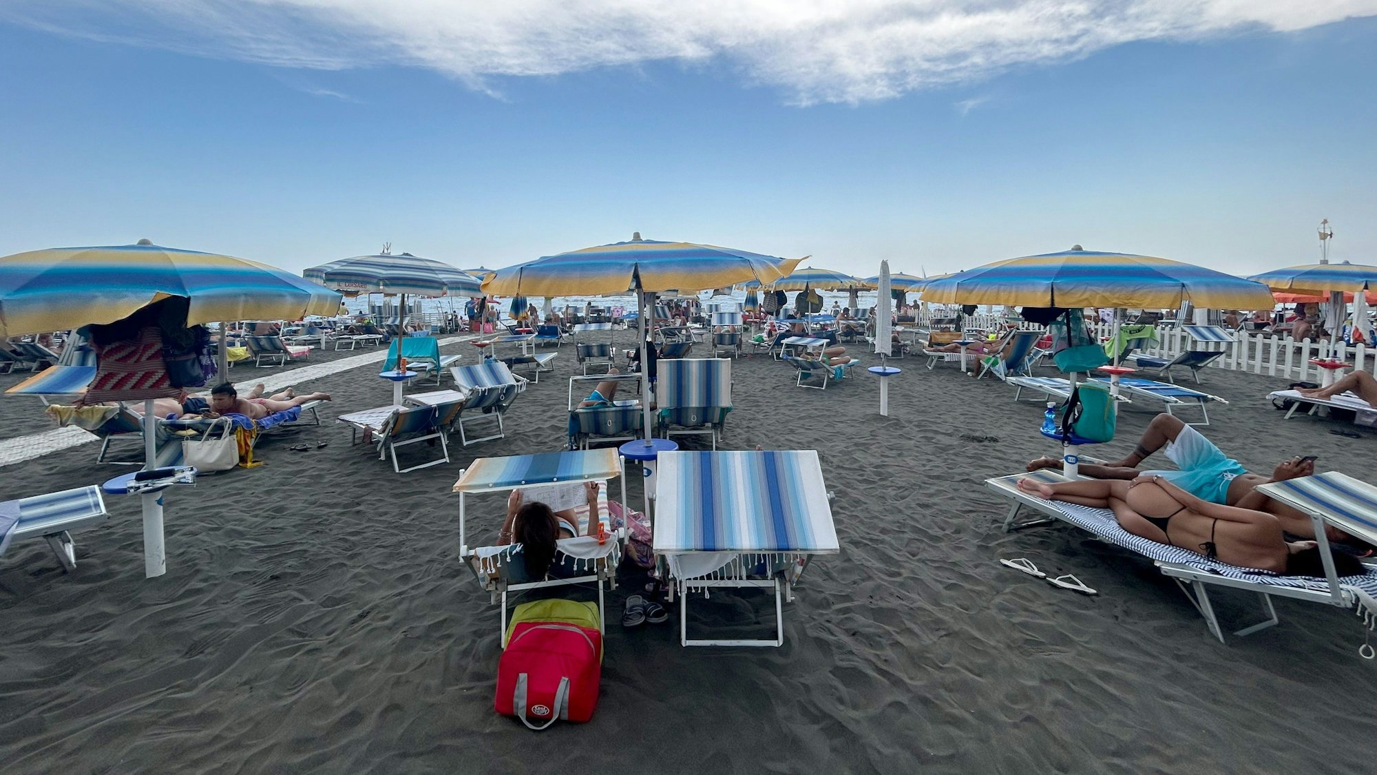 Menschen liegen auf Strandliegen unter Sonnenschirmen am Mittelmeer.