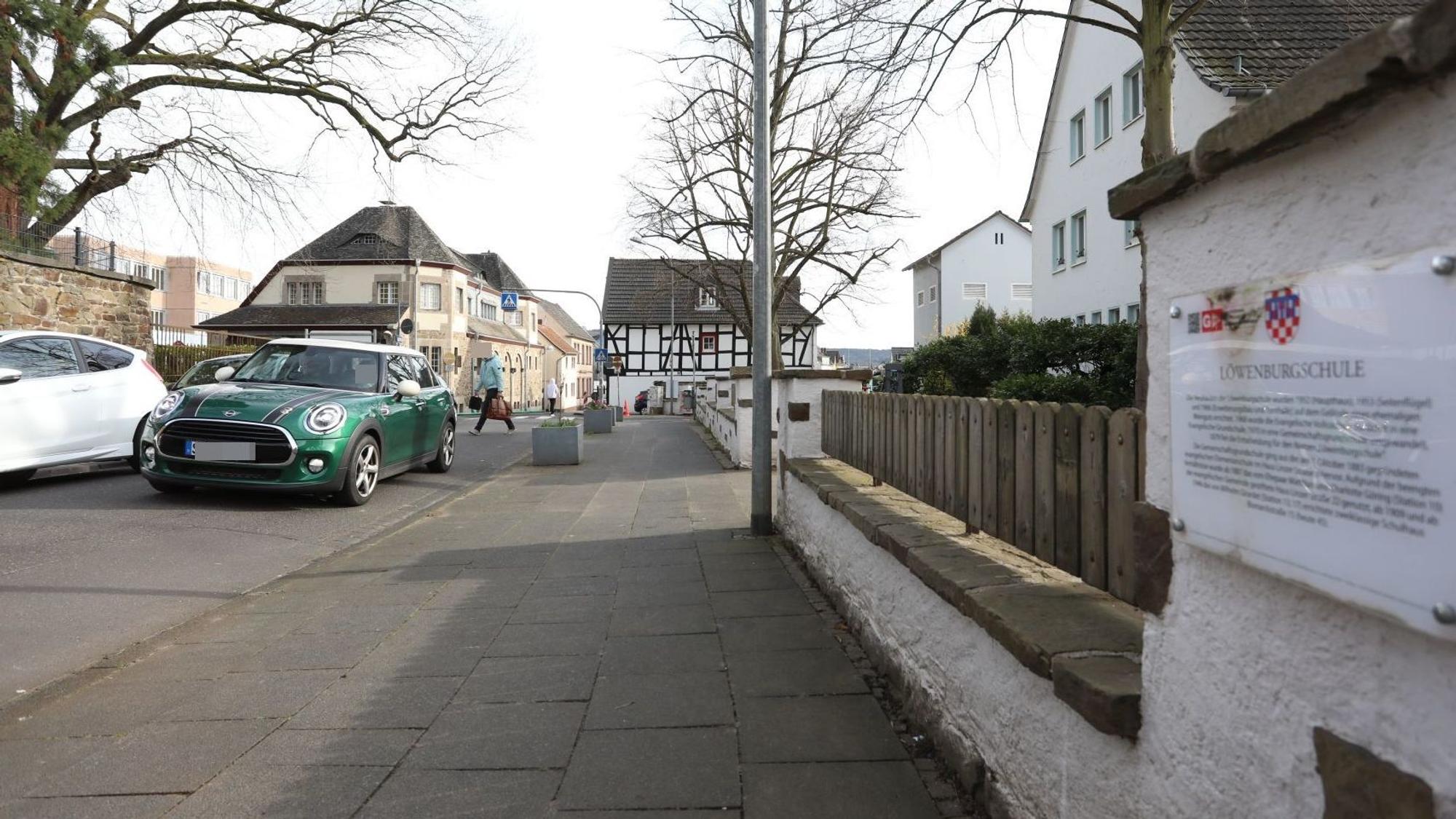 Ein grünes Auto auf einer Straße, im Hintergrund quert ein Fußgänger die Fahrbahn.