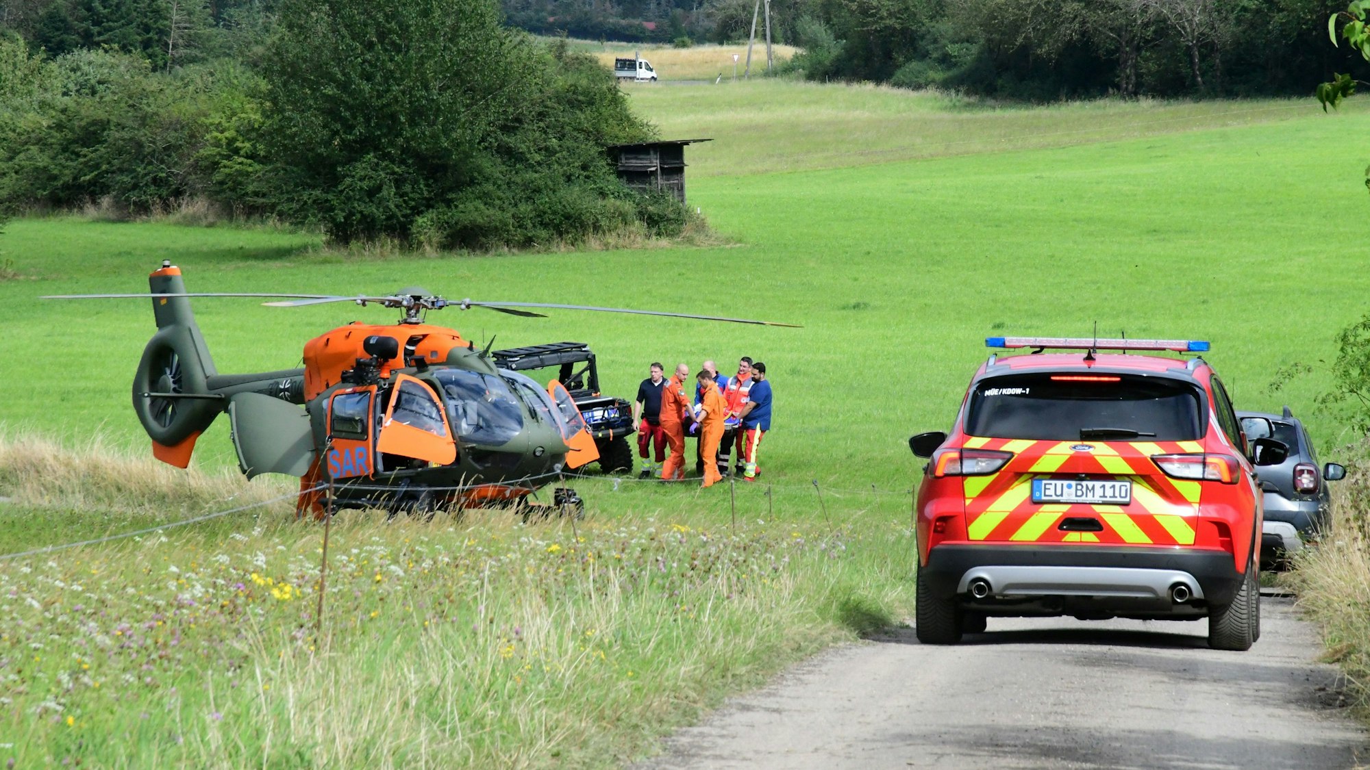 Von einem Quad der Bergwacht wird der Verletzte in den Rettungshubschrauber geladen. Rechts steht ein Feuerwehrfahrzeug.