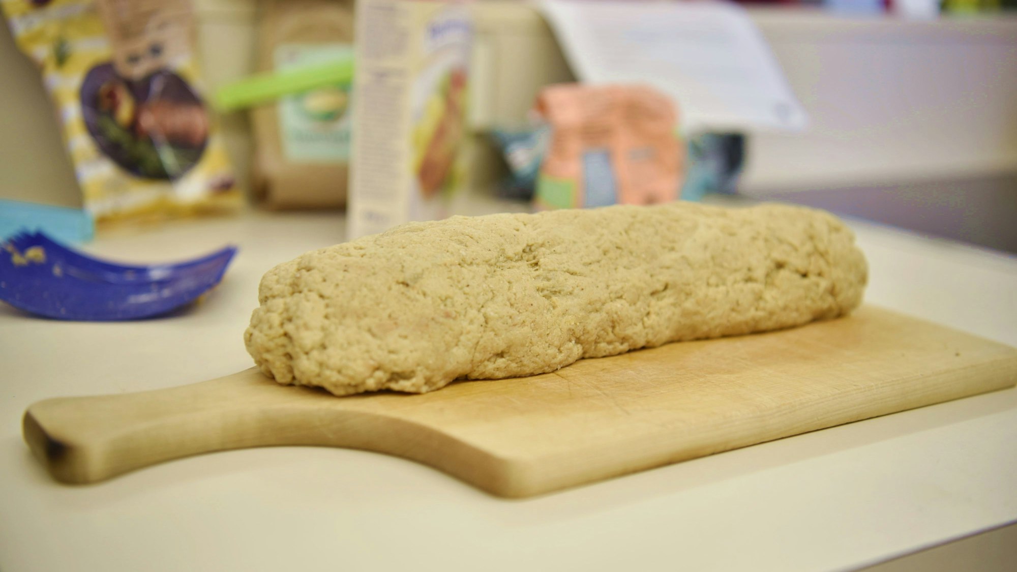 Ein Strang Seitan-Teig liegt auf einem Holzbrett auf einer Küchenarbeitsplatte.