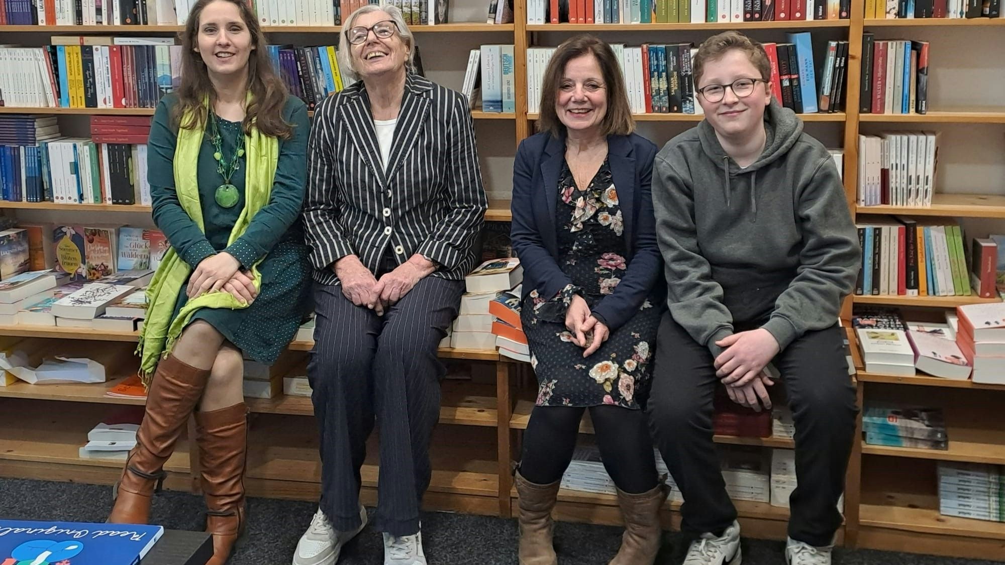 Drei Frauen und ein junger Mann lächeln in die Kamera. Hinter ihnen sind Bücherregale zu sehen.