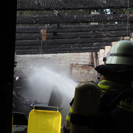 Mit einem Wasserstrahl kühlt ein Feuerwehrmann eine Flasche mit Acetylen bei einem Brand in Antweiler.