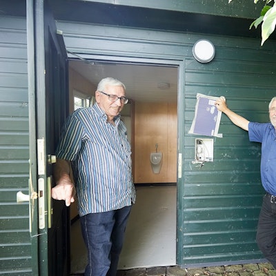 Heinz Schmitz und Gerhard Mayer stehen am Eingang des Toilettenhäuschens. Dort ist der Münzautomat aus der Wand gerissen.