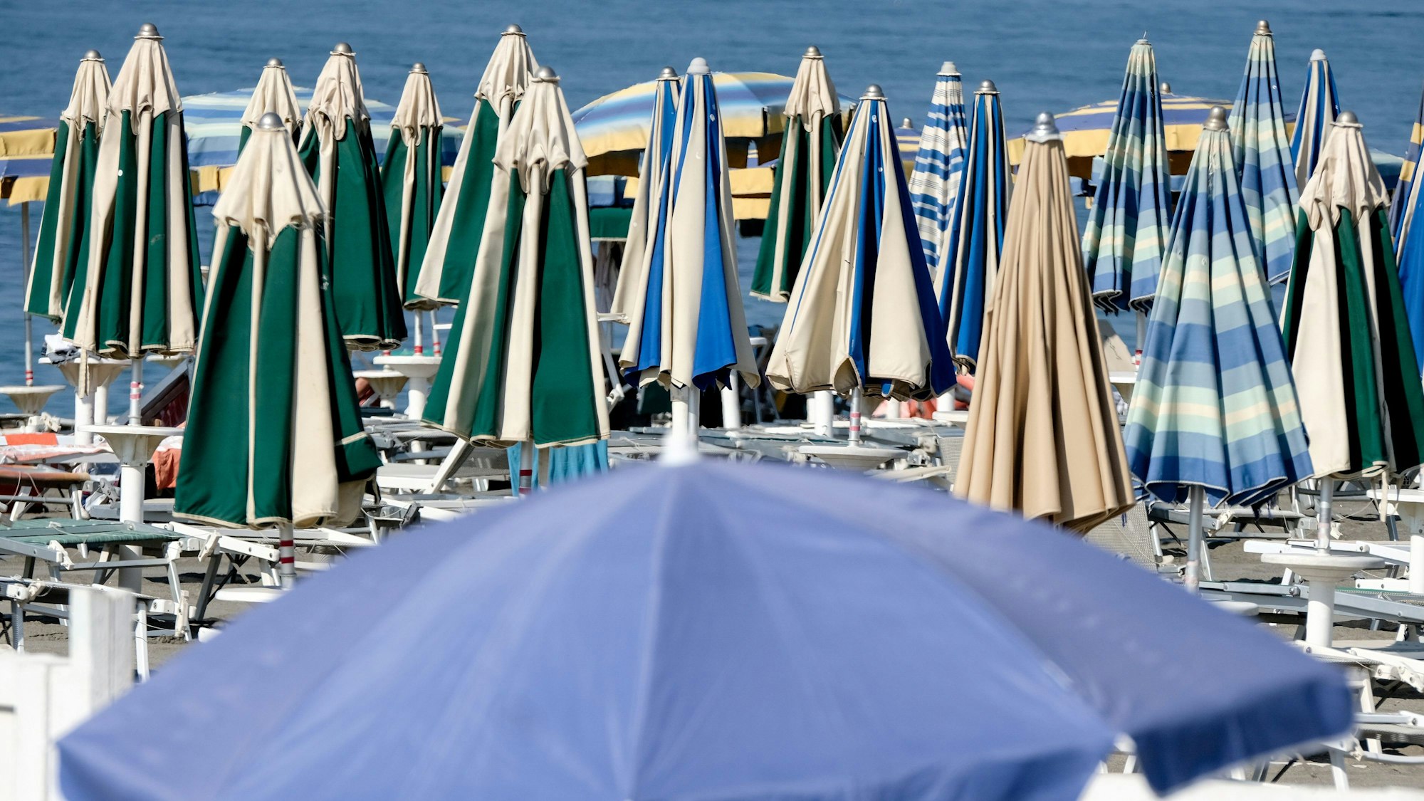 Sonnenschirme stehen geschlossen am Strand.
