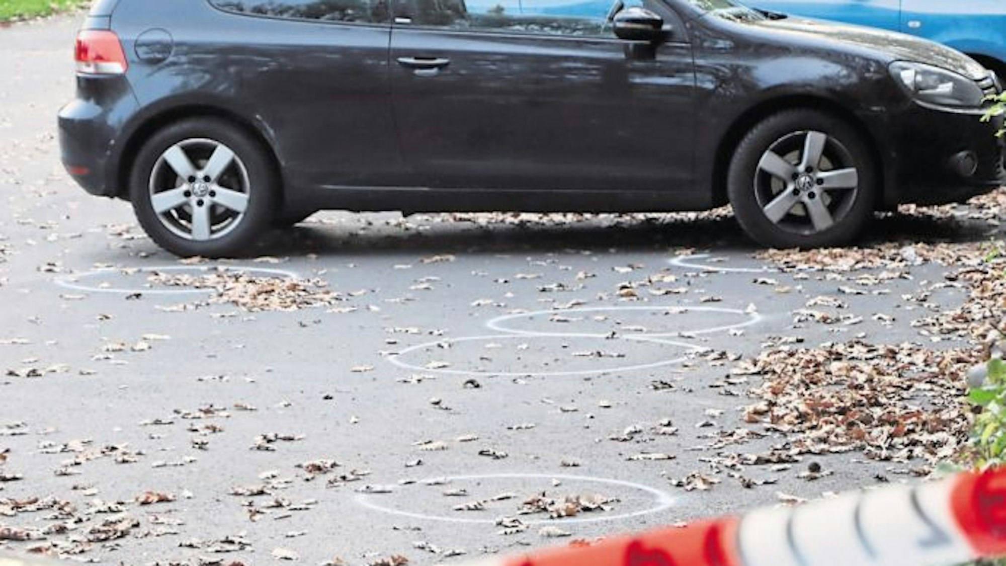 Auf dem Bild ist der Parkplatz zu sehen, auf dem ein Mann in Hürth eine Frau mit Schüssen verletzte. Auf dem Boden sind mit Kreise kreise eingezeichnet. Es parken Autos dort, der Platz ist abgesperrt.
